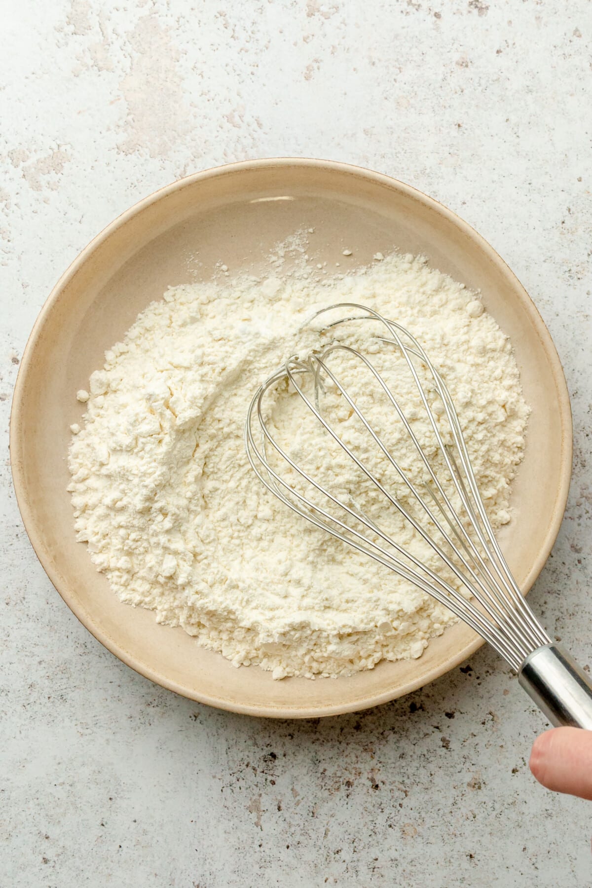 Dry ingredients are whisked in a shallow ceramic bowl on a light grey surface.