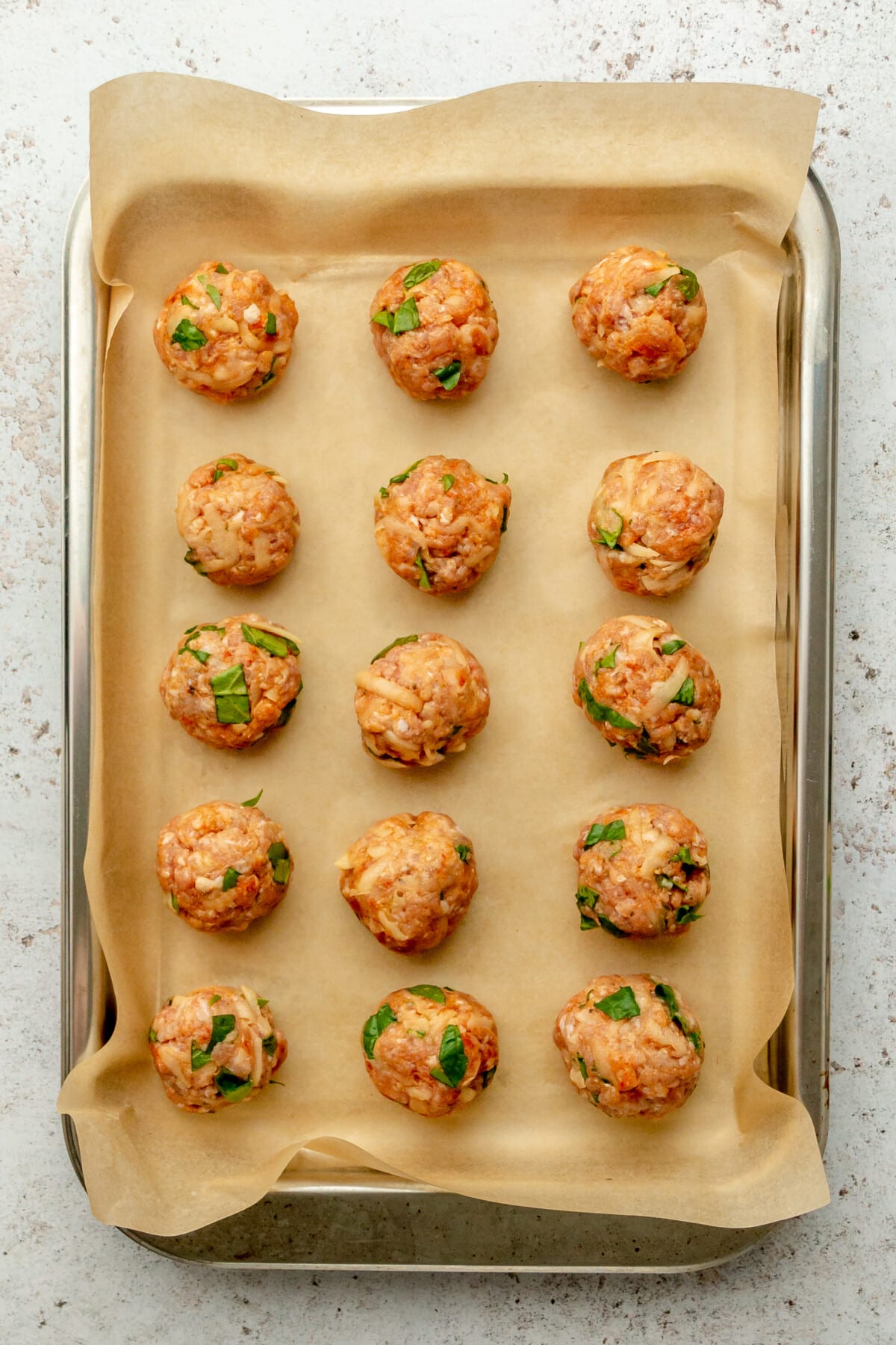 Raw chorizo potato meatballs sit on a lined and rimmed stainless steel tray on a light grey surface.