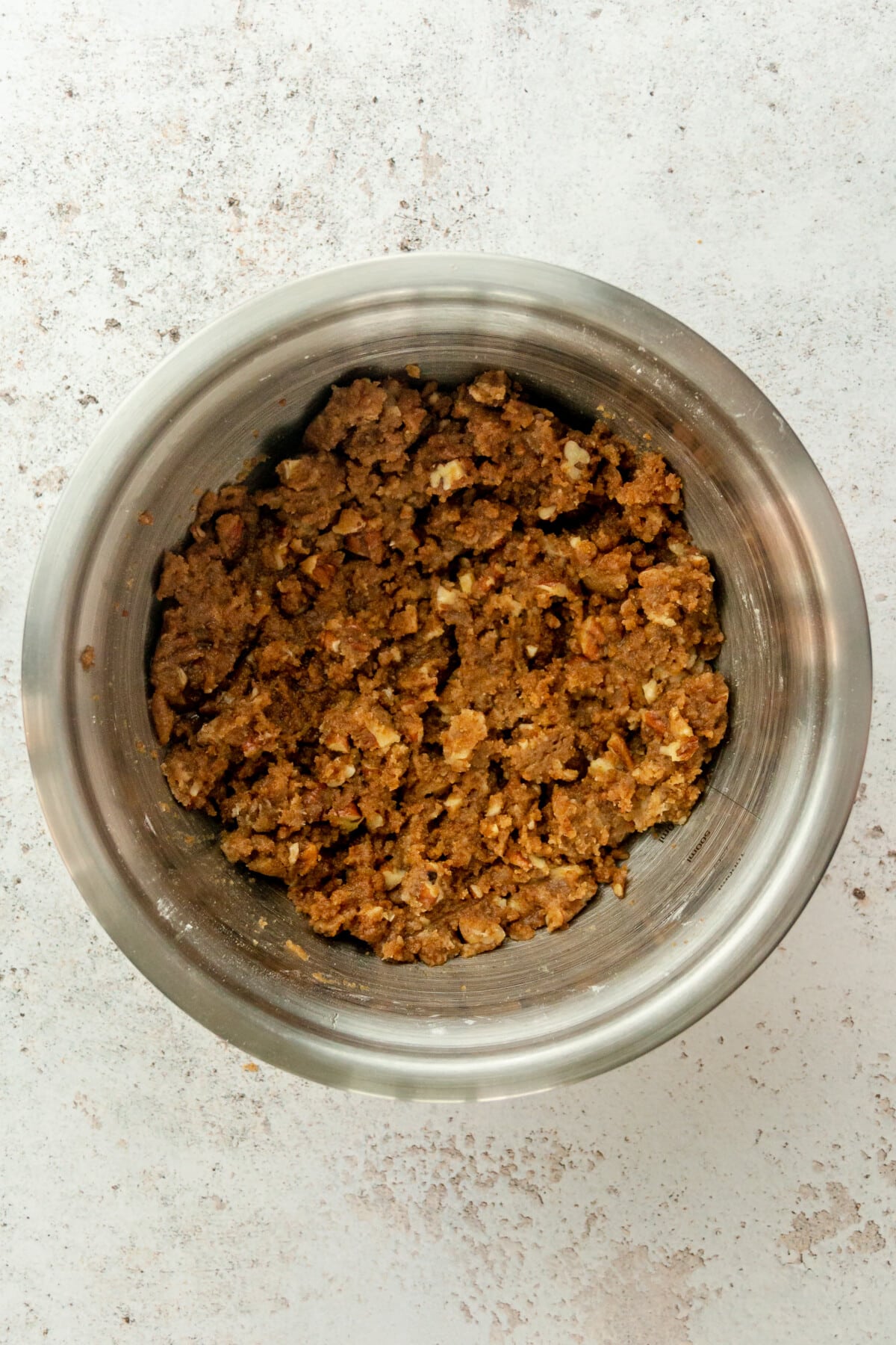 A crumb mixture sits in a stainless steel bowl on a light grey surface.