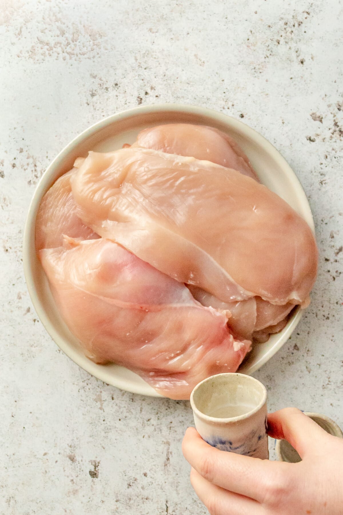 A person seasoning thin cut chicken breasts with salt and pepper.