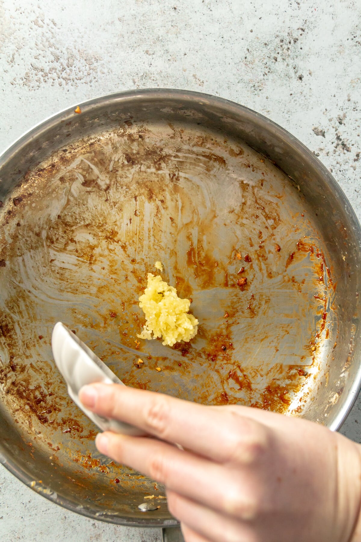 A person adding minced garlic to a stainless steel skillet.