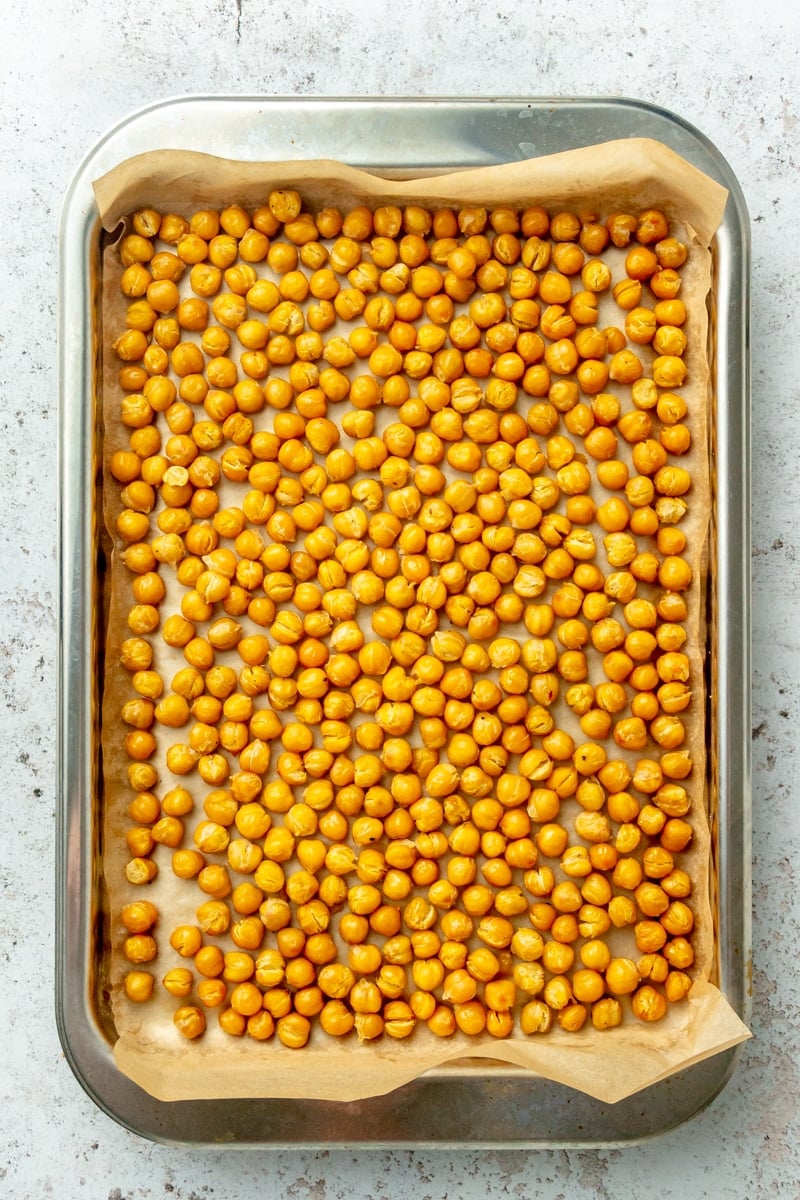 Crispy roasted chickpeas sit on a parchment lined baking sheet.