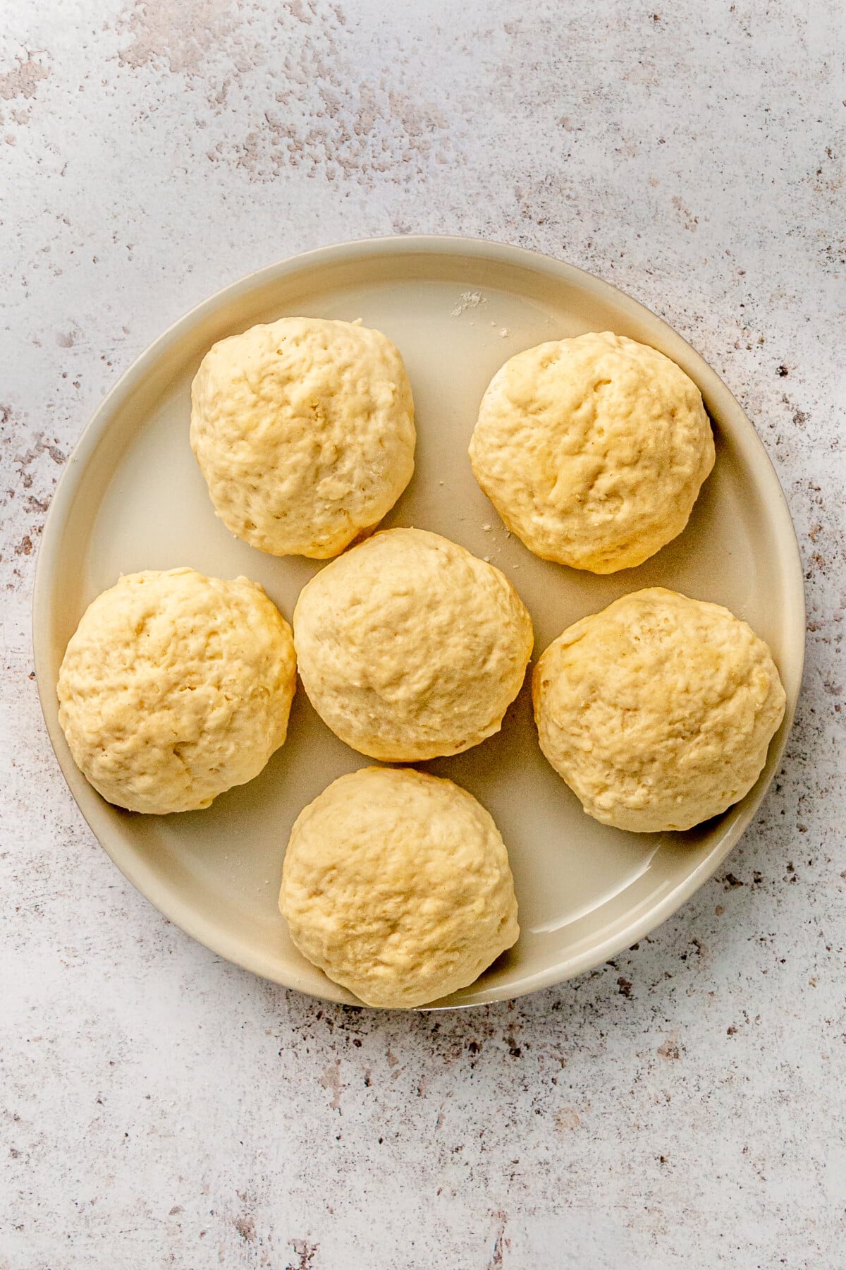 Six small pizza doughs sit ona gray plate on a light grey surface.