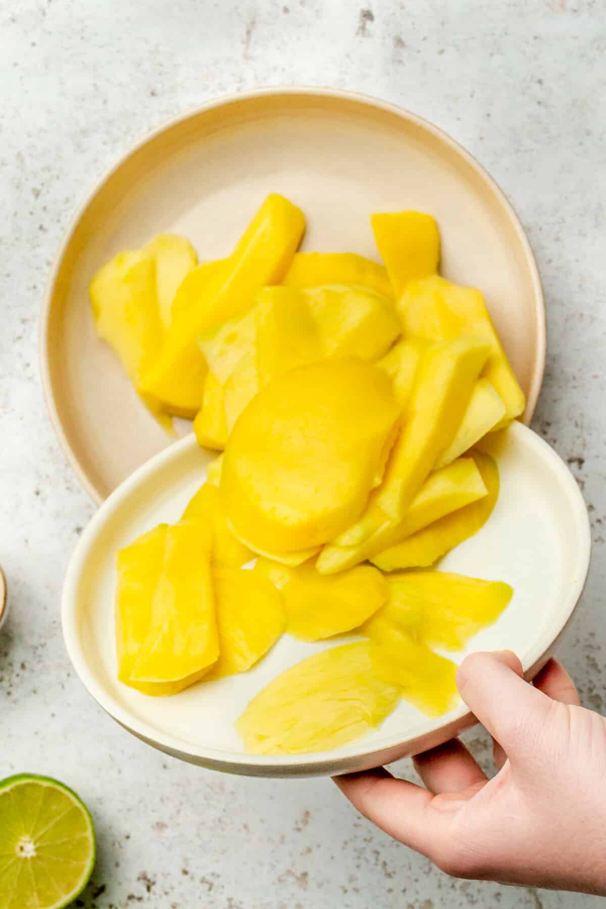 Slices of mango are tossed into a shallow bowl on a light grey colored surface.