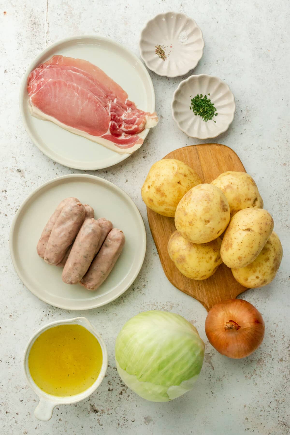 Ingredients for Dublin coddle sit in a variety of bowls and plates on a light grey surface.