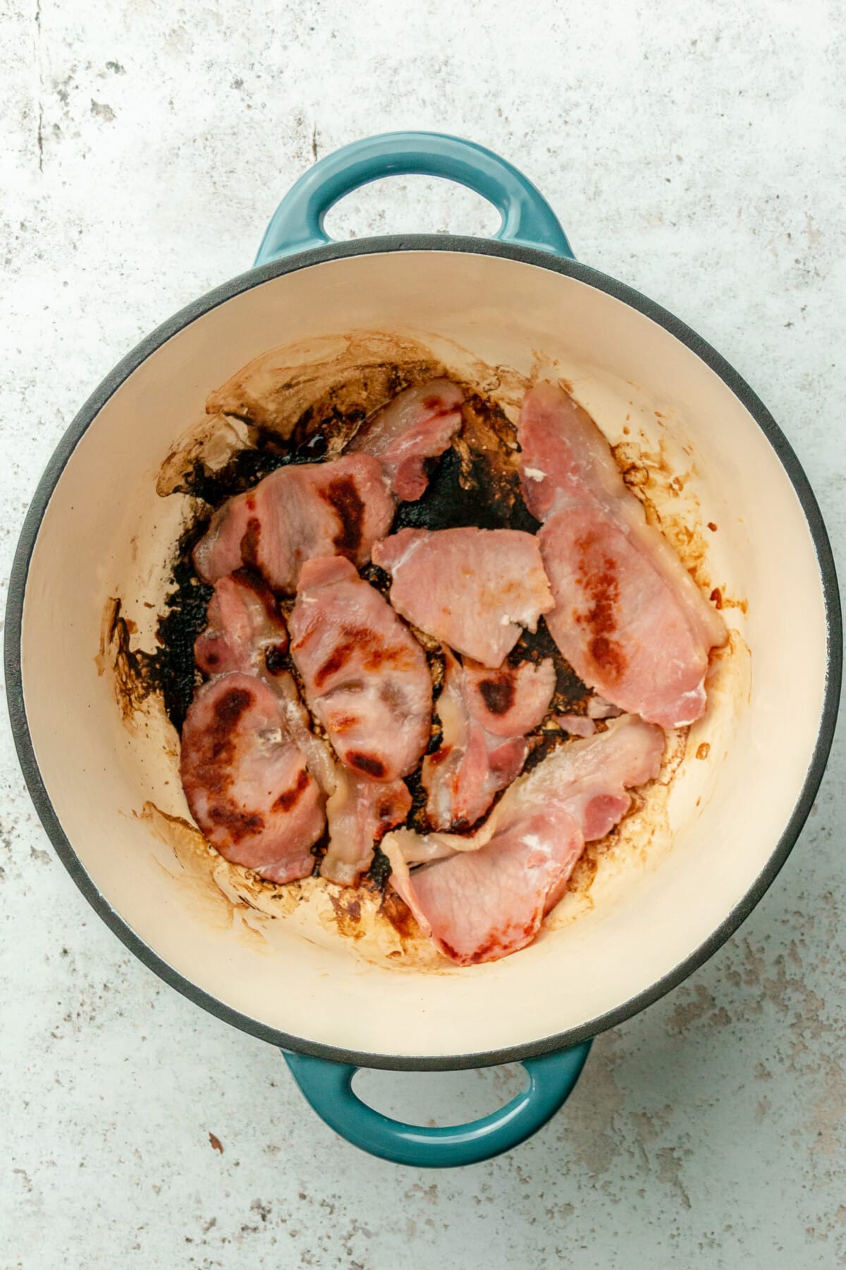 Cooked bacon sits in a Dutch oven on a light gray surface.