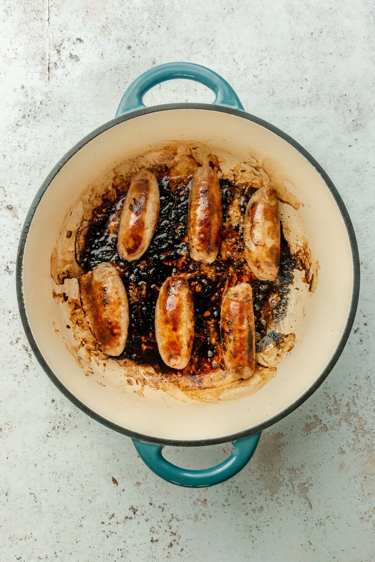 Cooked sausages sit in a Dutch oven on a light gray surface.