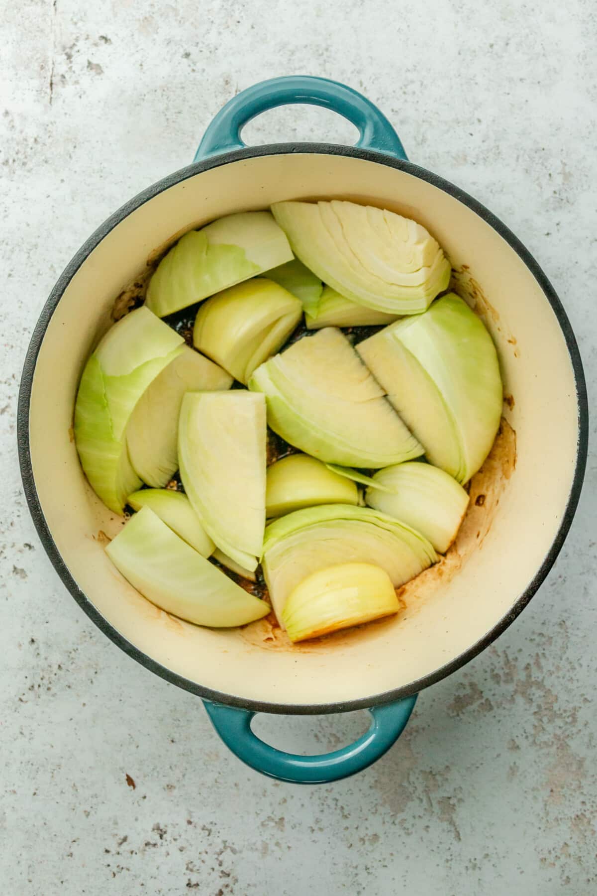 Wedges of cabbage sit in a Dutch oven on a light gray surface.