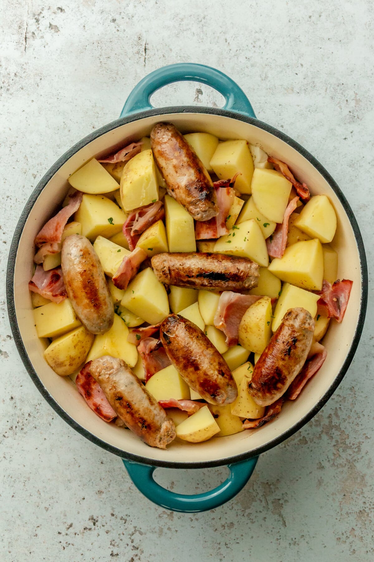 Unbaked Dublin Coddle sits in a Dutch oven on a light gray surface.