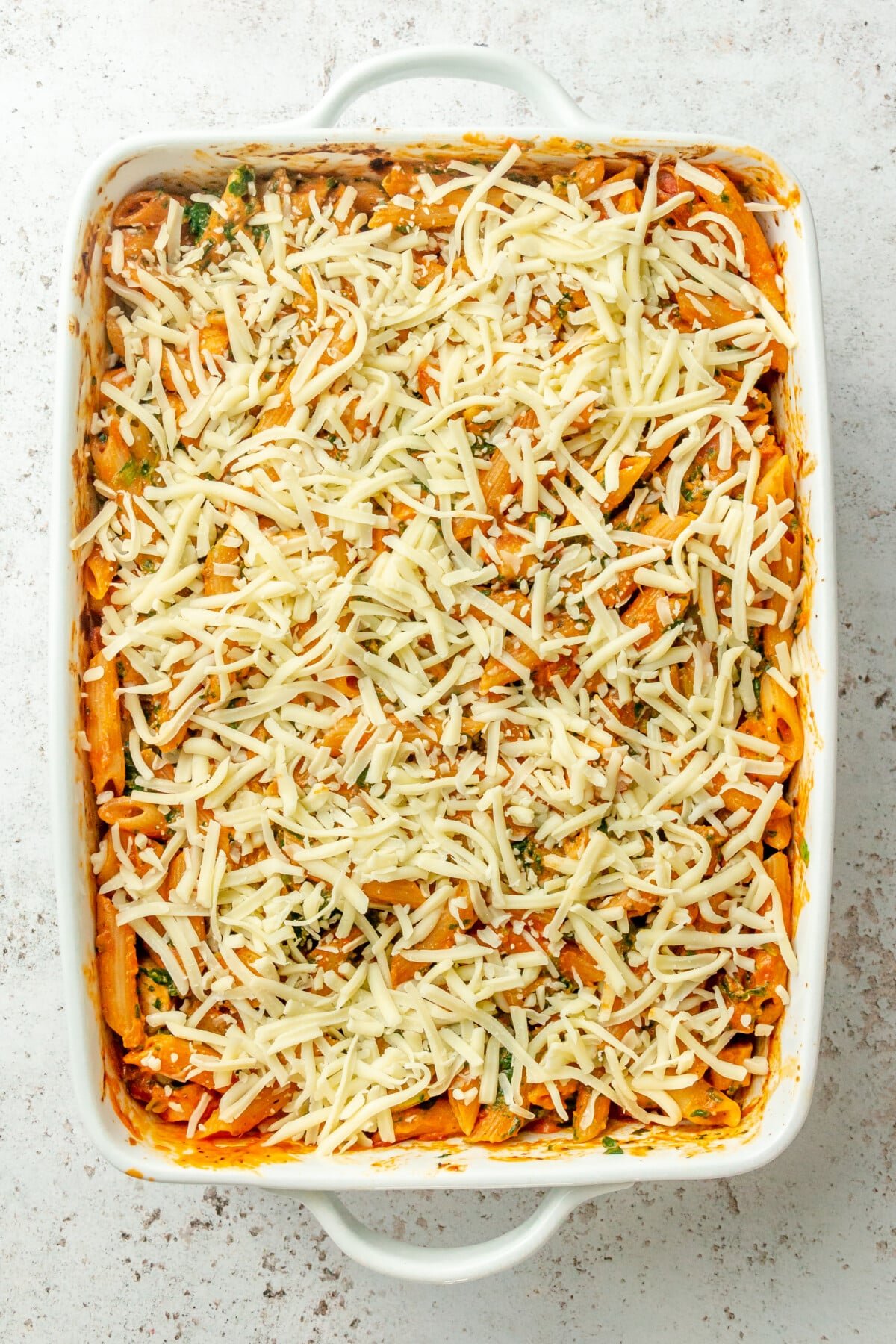 Grated cheese sits on top of a no boil pasta bake on a light grey colored surface.