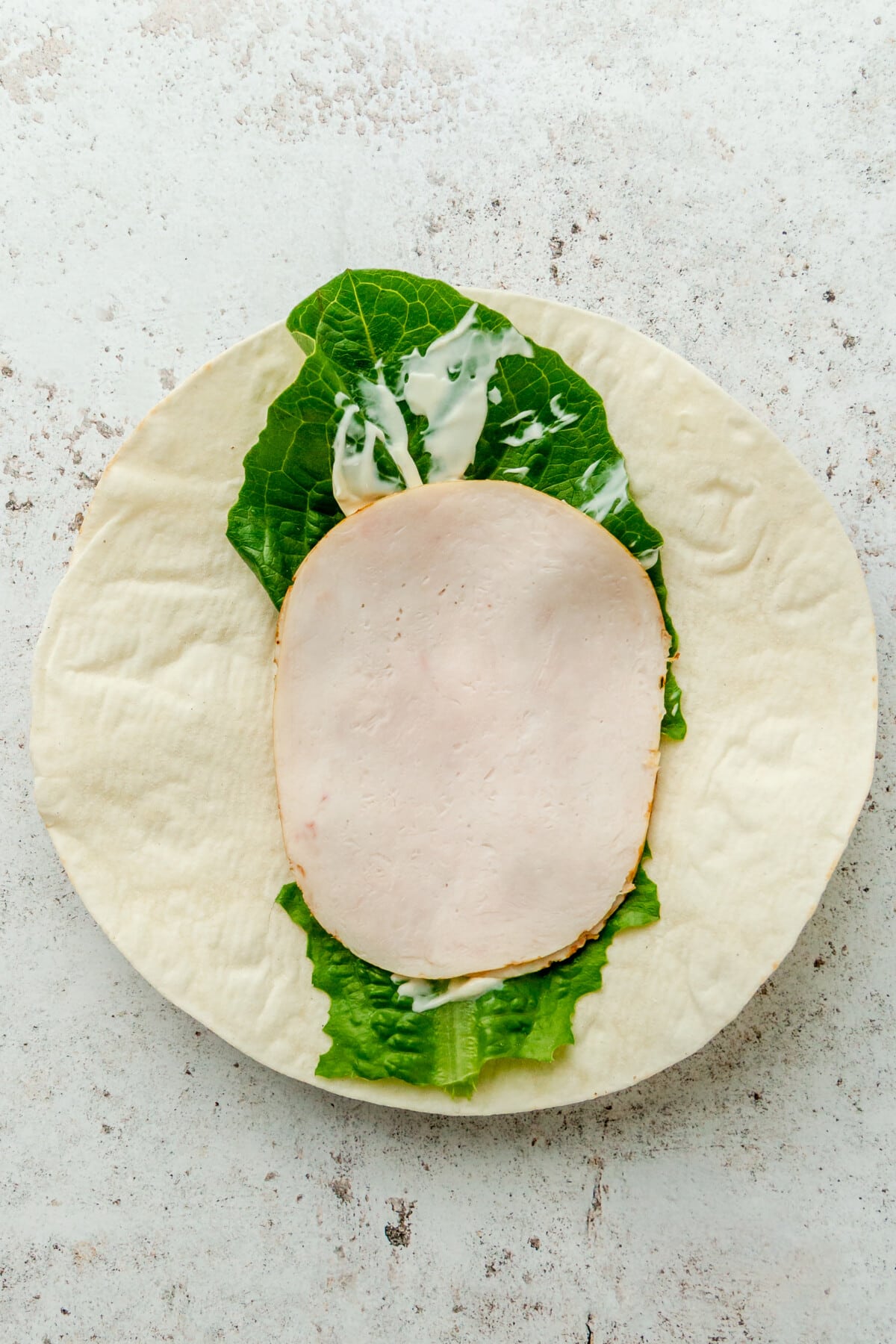 A slice of turkey sits on top of a romaine leaf on a light grey surface.