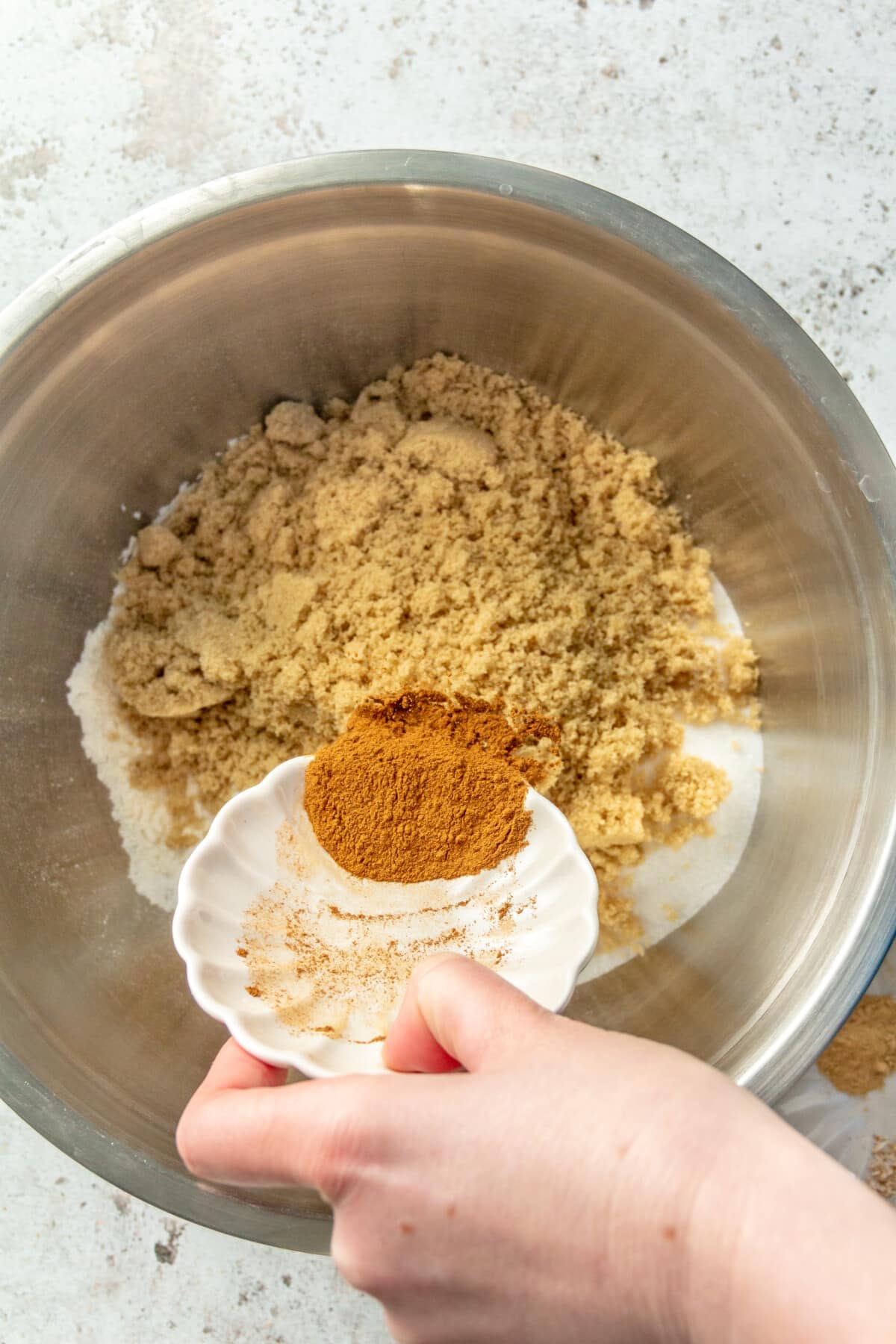A variety of dry ingredients are shown being added into a large metal mixing bowl.