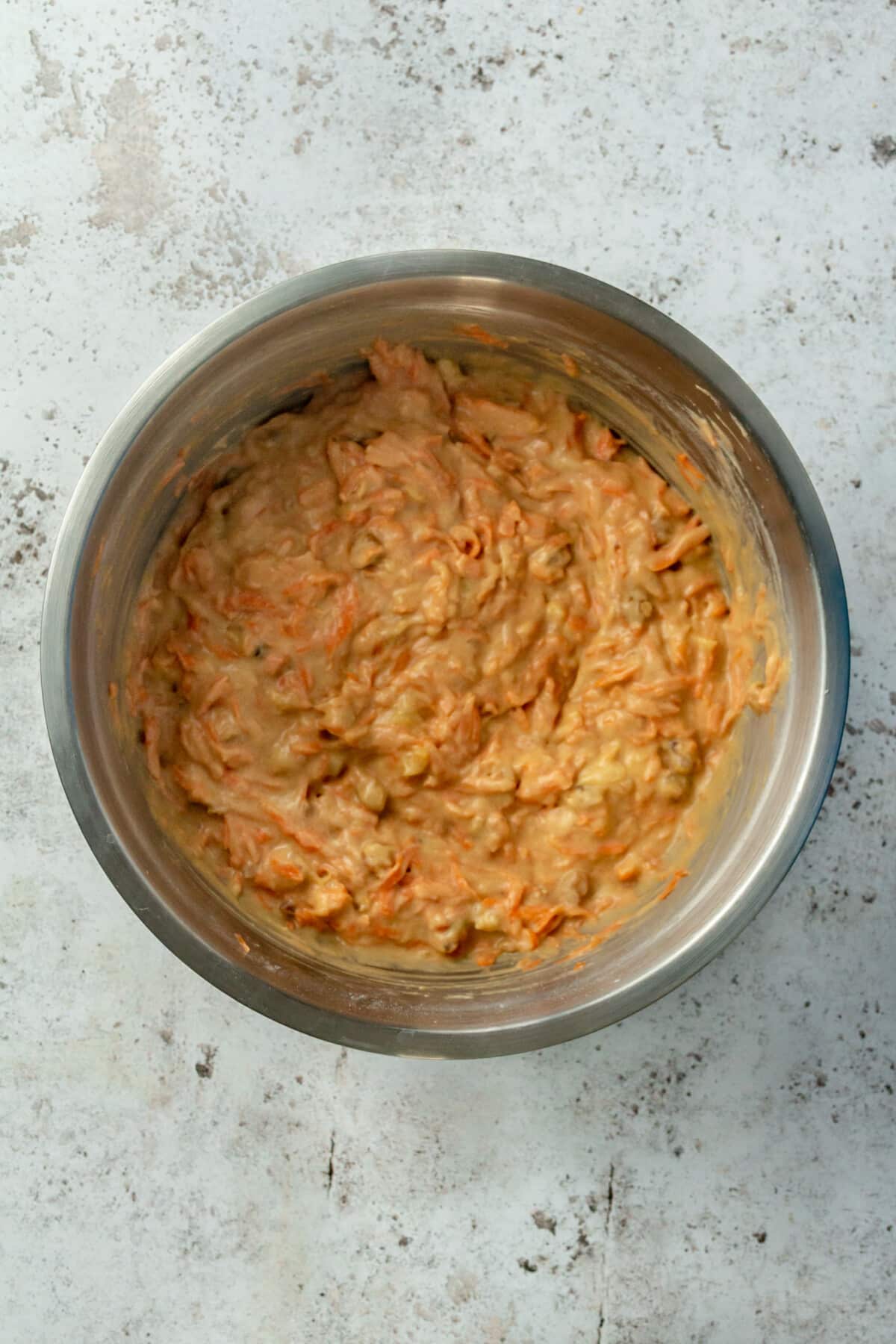 Carrot cake batter sits in a large metal mixing bowl.