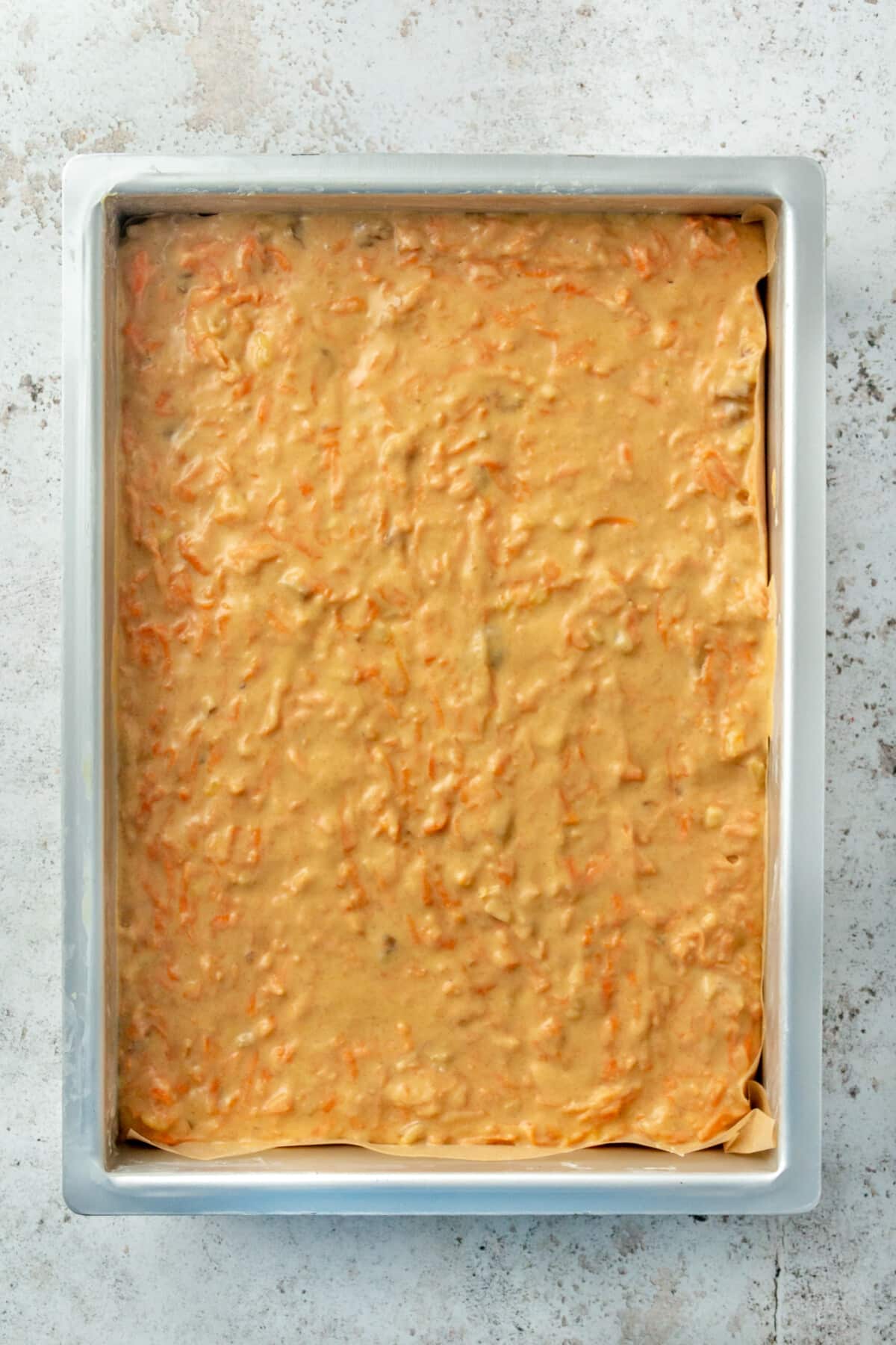 Carrot cake batter is shown sitting in a parchment lined baking pan.