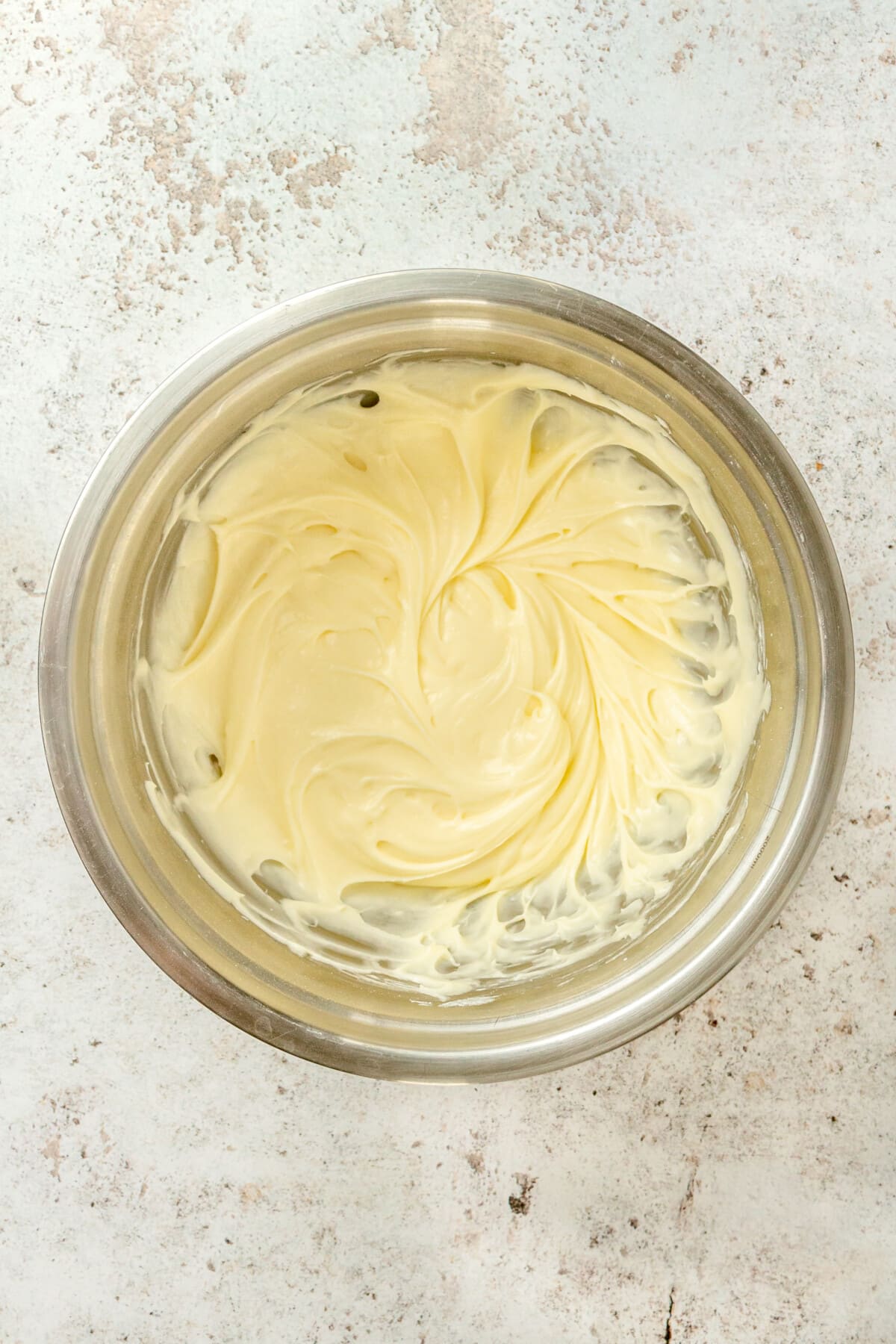 Cream cheese icing sits in a large metal mixing bowl.