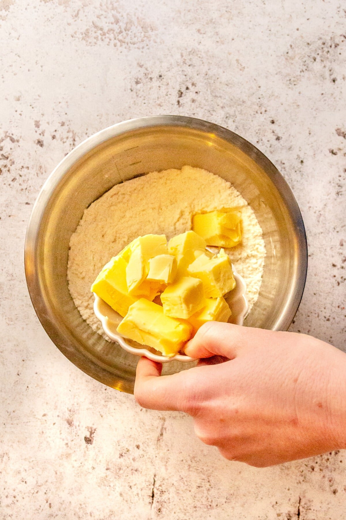 Cubes of butter are shown being added to a metal mixing bowl of flour.