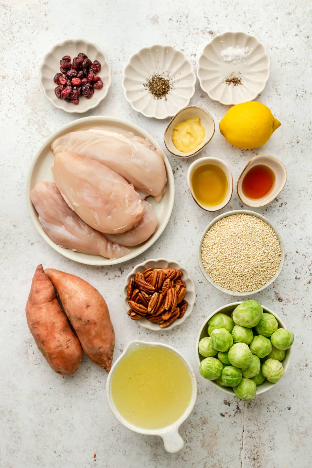 Ingredients for harvest quinoa bowls with chicken and sweet potatoes sit in a variety of bowls and plates on a light grey surface.