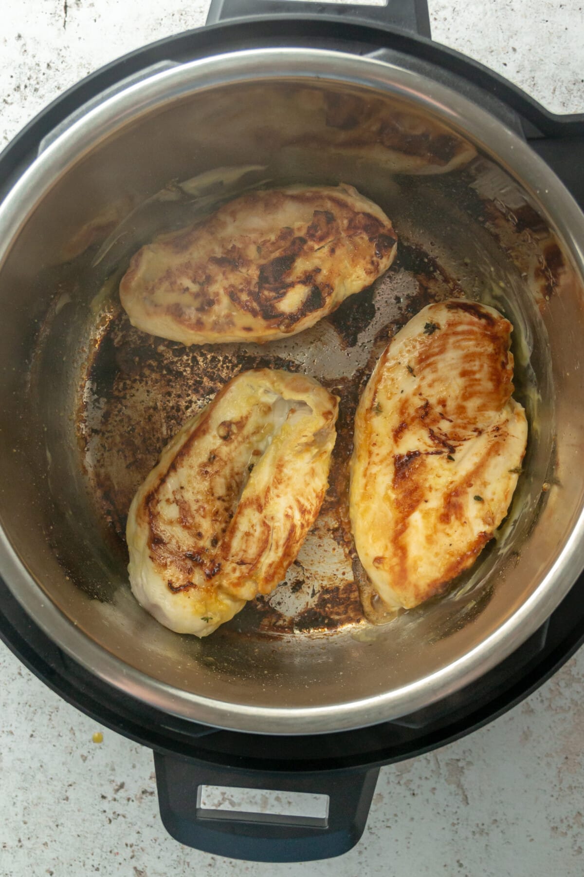Chicken breast fillets are cooked and golden in an instant pot on a light grey colored surface.
