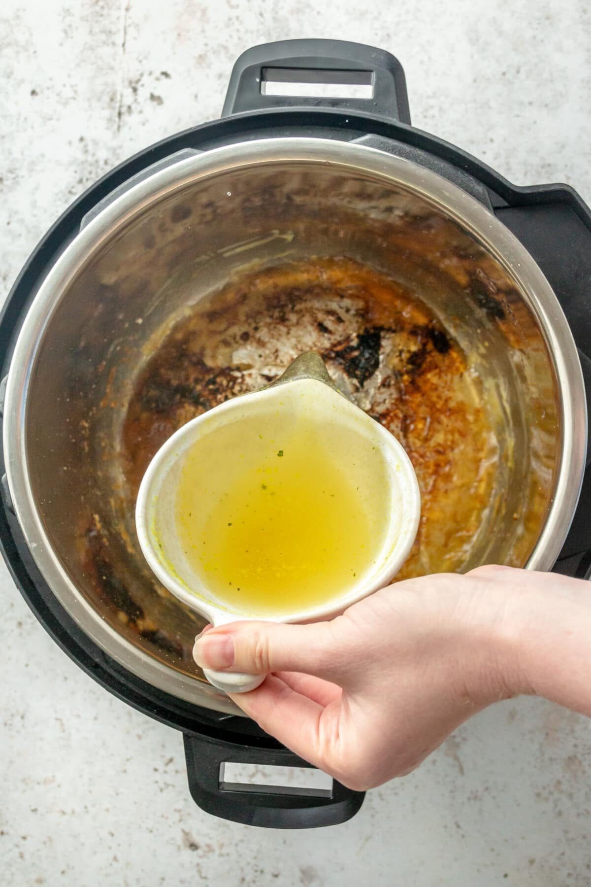 Chicken broth is poured into an instant pot, whilst sitting on a light grey colored surface.