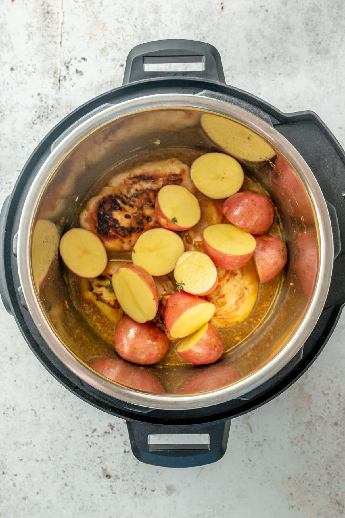 Red potatoes have been placed on top of chicken fillets inside an instant pot, sitting on a light grey colored surface.