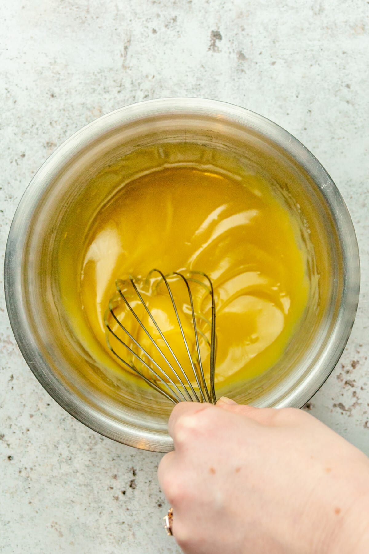 A honey mustard sauce is whisked in a stainless steel bowl on a light gray surface.