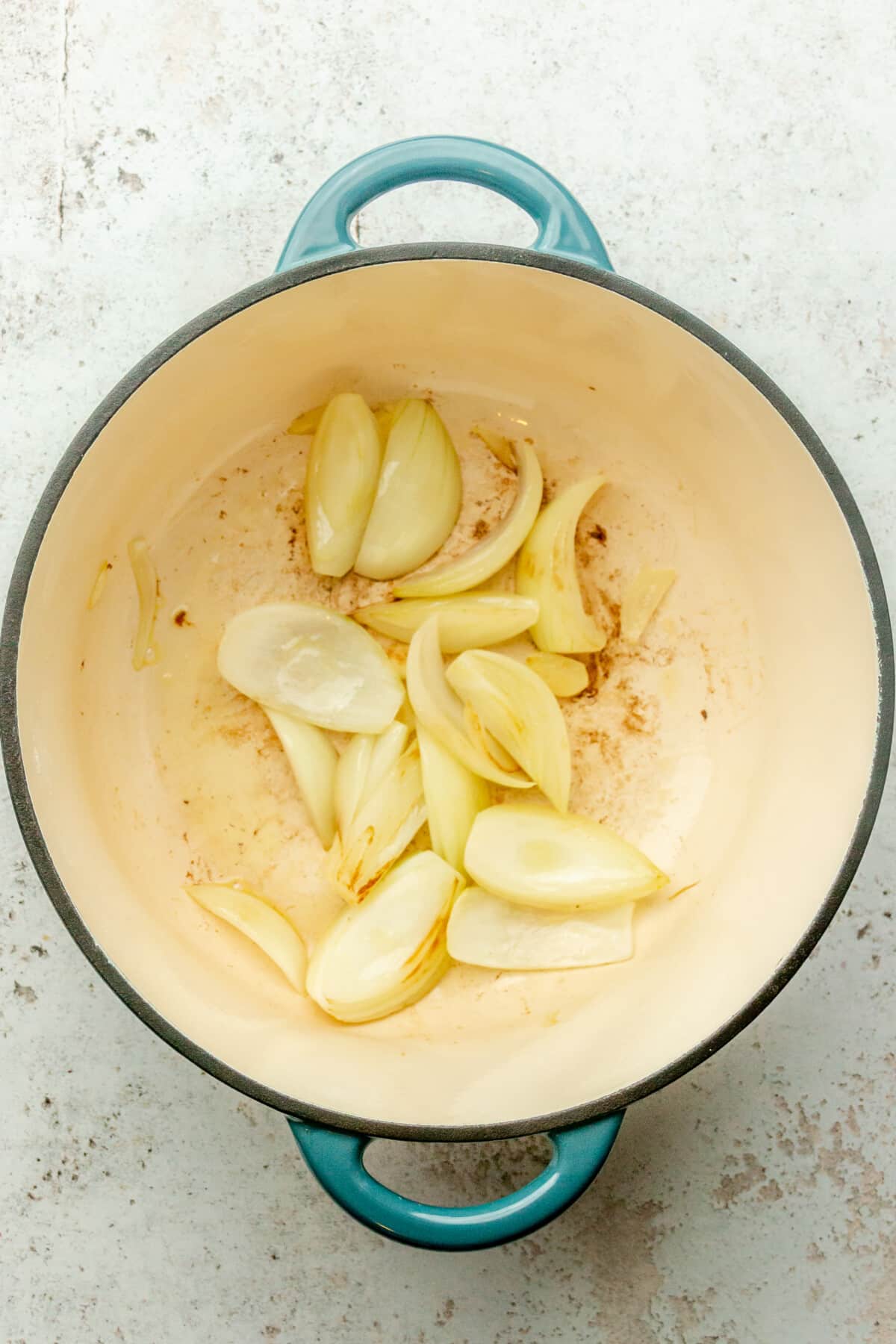 Cooked onion wedges sit in a Dutch oven on a light gray surface.