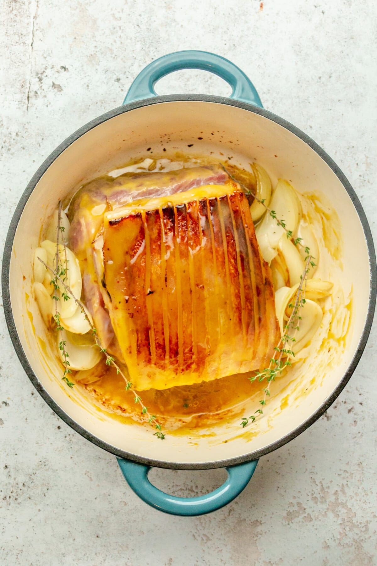 A seared pork loin sits in a Dutch oven on a light gray surface surrounded by broth and onion wedges.