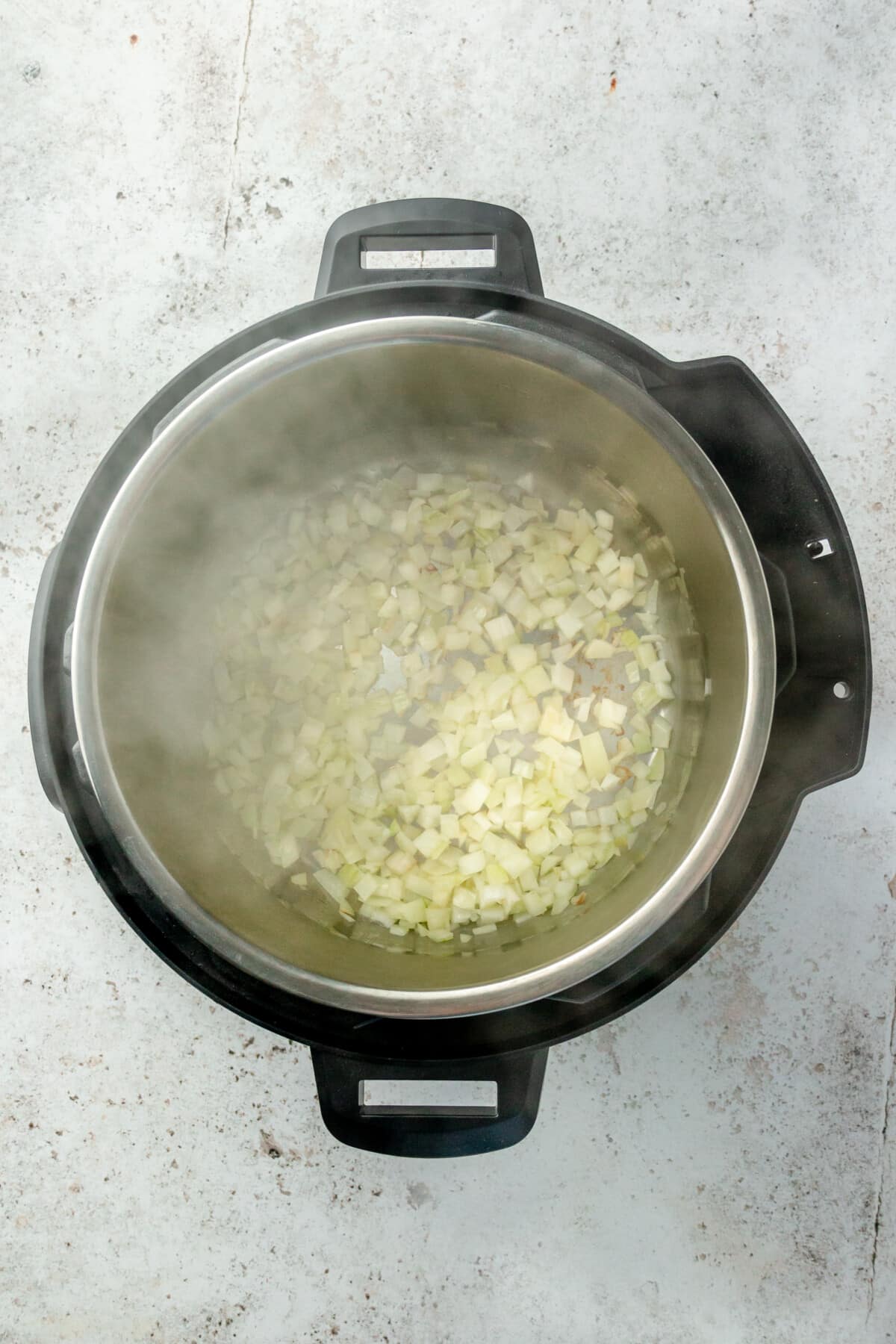 Steam is visible from a hot instant pot with diced onion cooked sitting atop on a light grey colored surface.