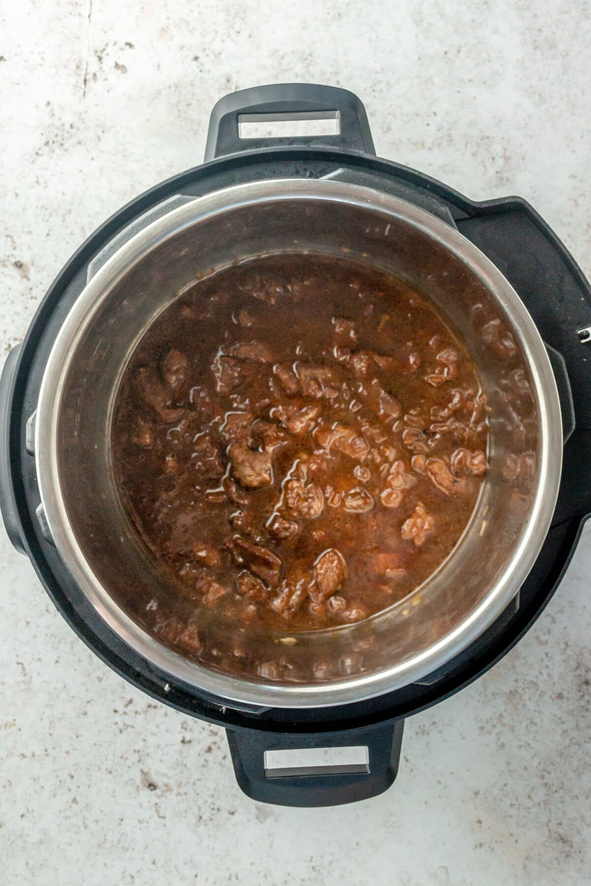 A beef stew mixture sits in an instant pot on a light grey colored surface.