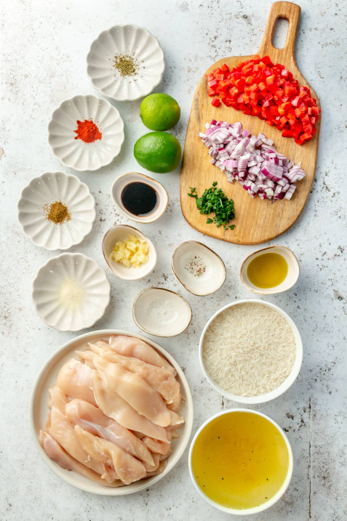 Ingredients for instant pot chicken fajitas and rice sit in a variety of bowls on a concrete surface.