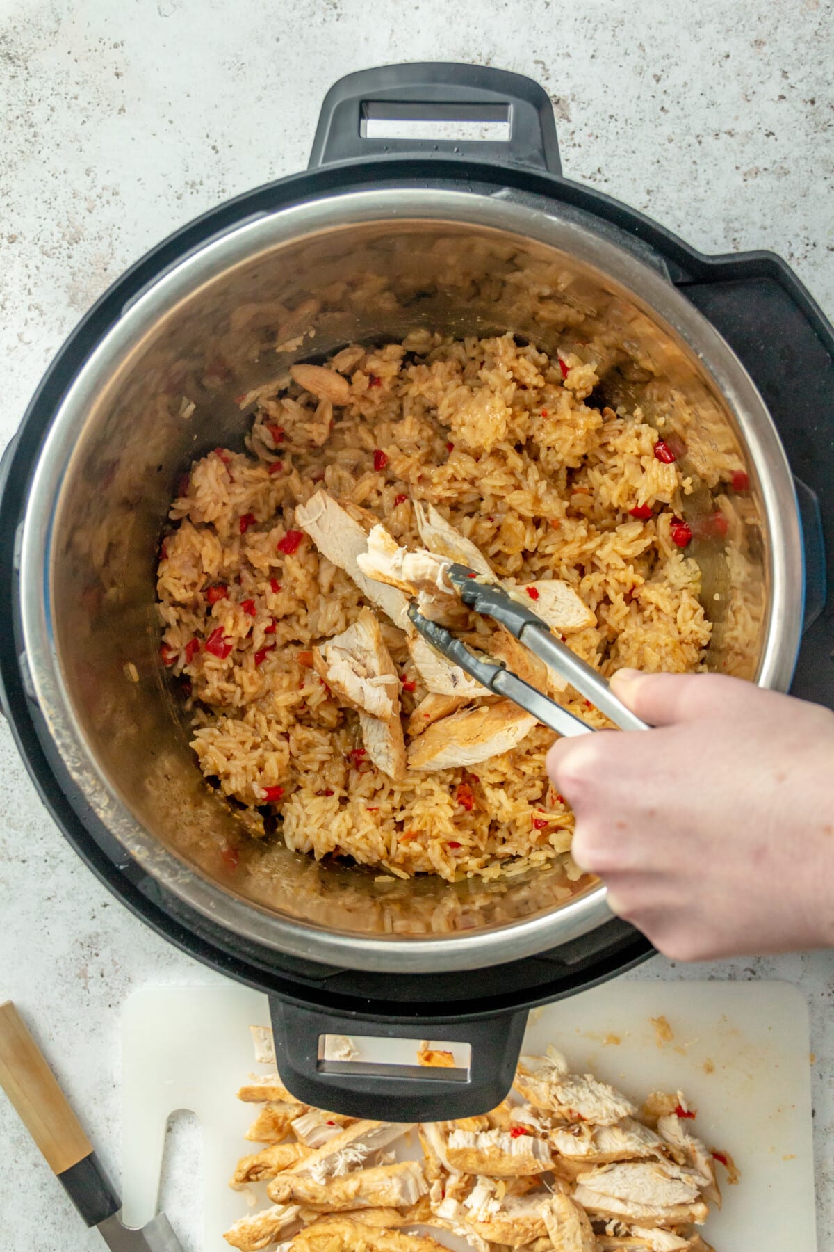 Strips of cooked chicken are shown being placed into an instant pot which holds a variety of other ingredients.