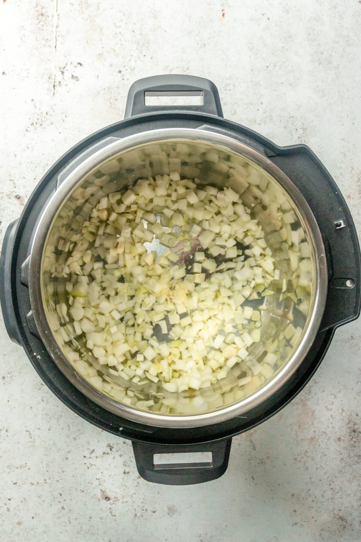 Finely diced onions sit in an instant pot on a light grey surface.