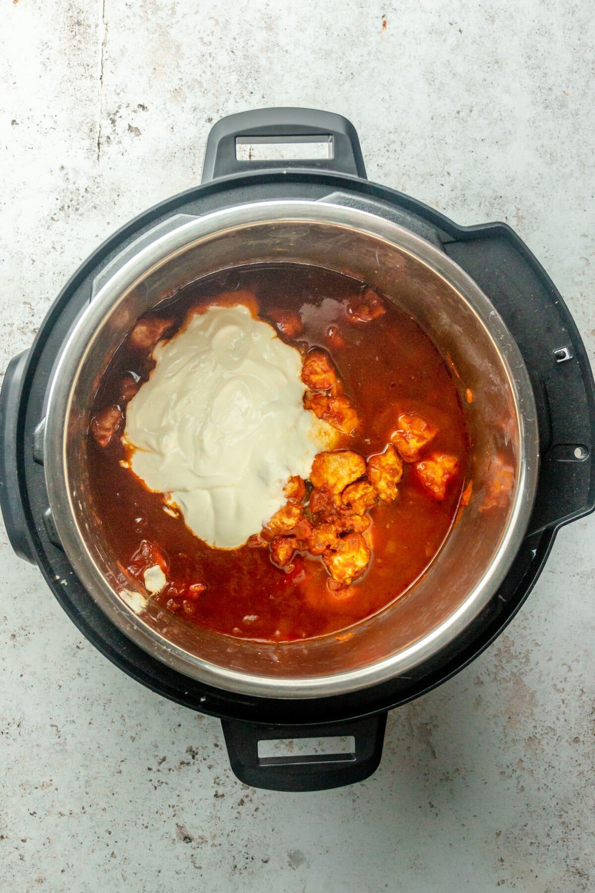 Yogurt sits on top of chicken tikka masala in an instant pot on a light grey surface.