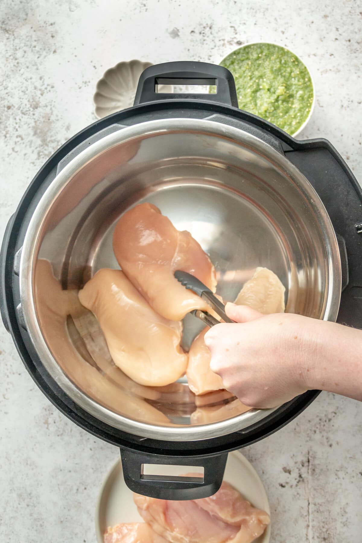Chicken breasts are placed into an instant pot sitting on a light grey surface.