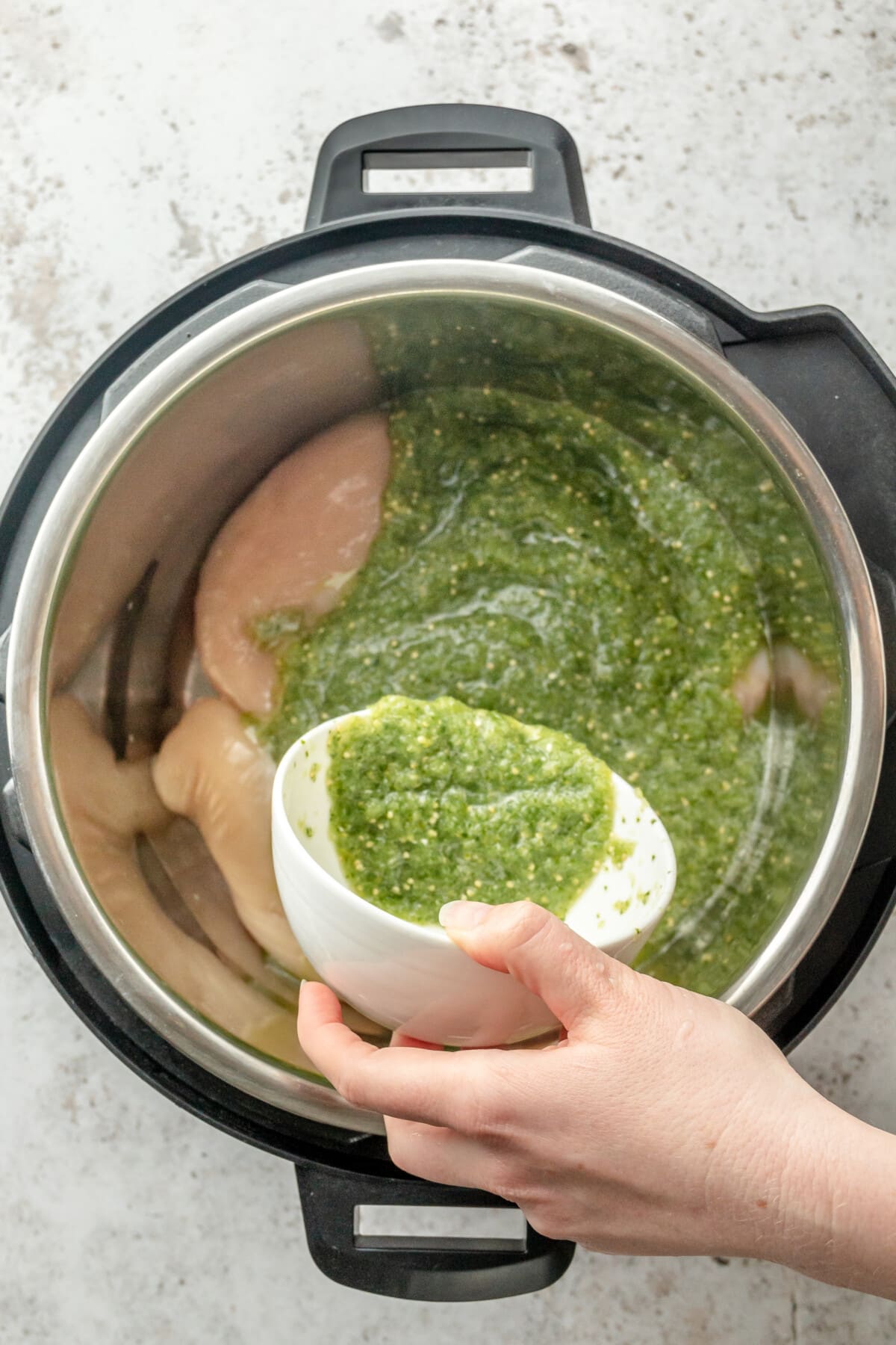 Salsa verde is poured over chicken breasts sitting in an instant pot on a light grey surface.