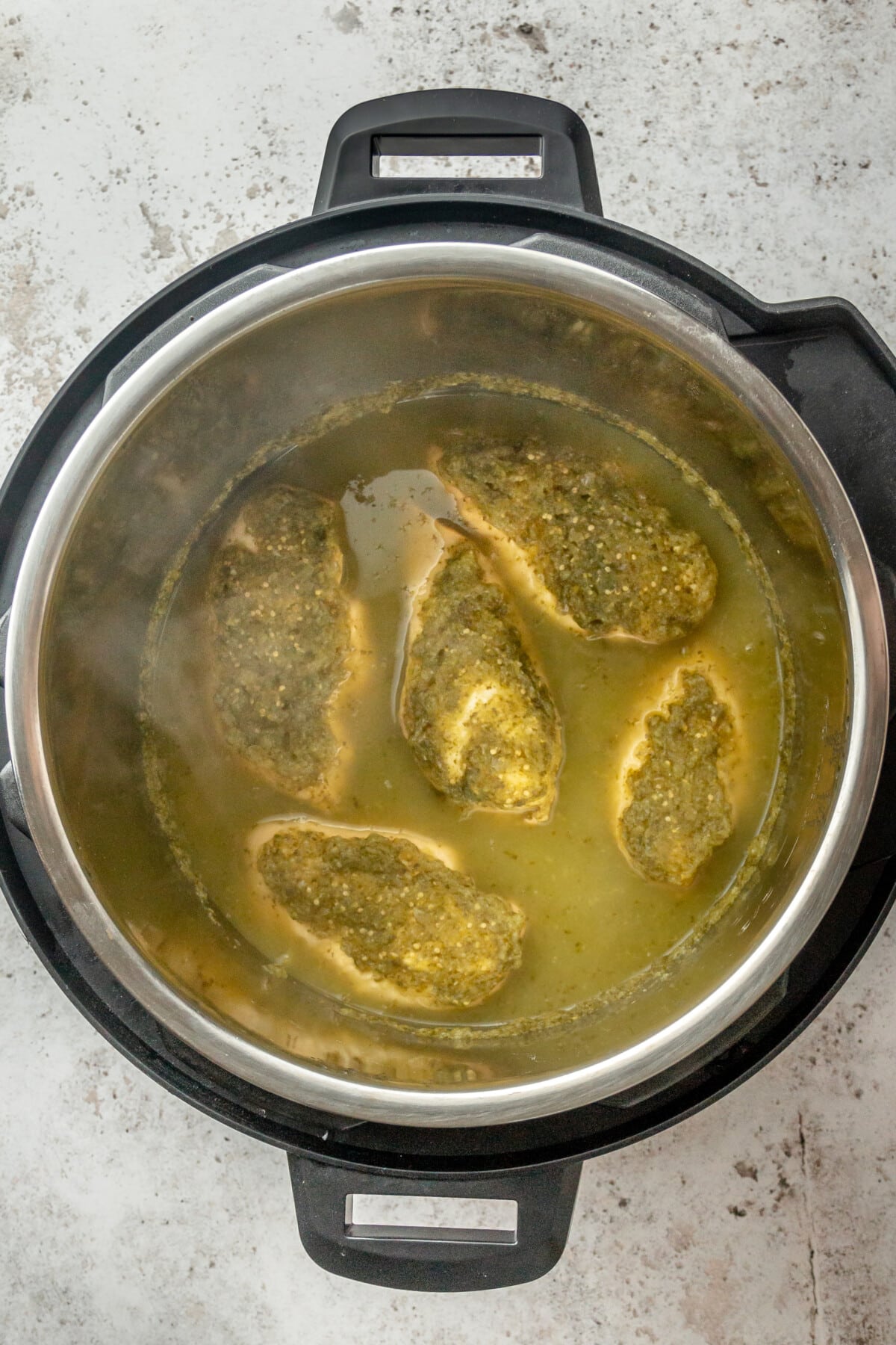 Salsa chicken breasts sit in an instant pot coated in salsa verde on a light grey surface.