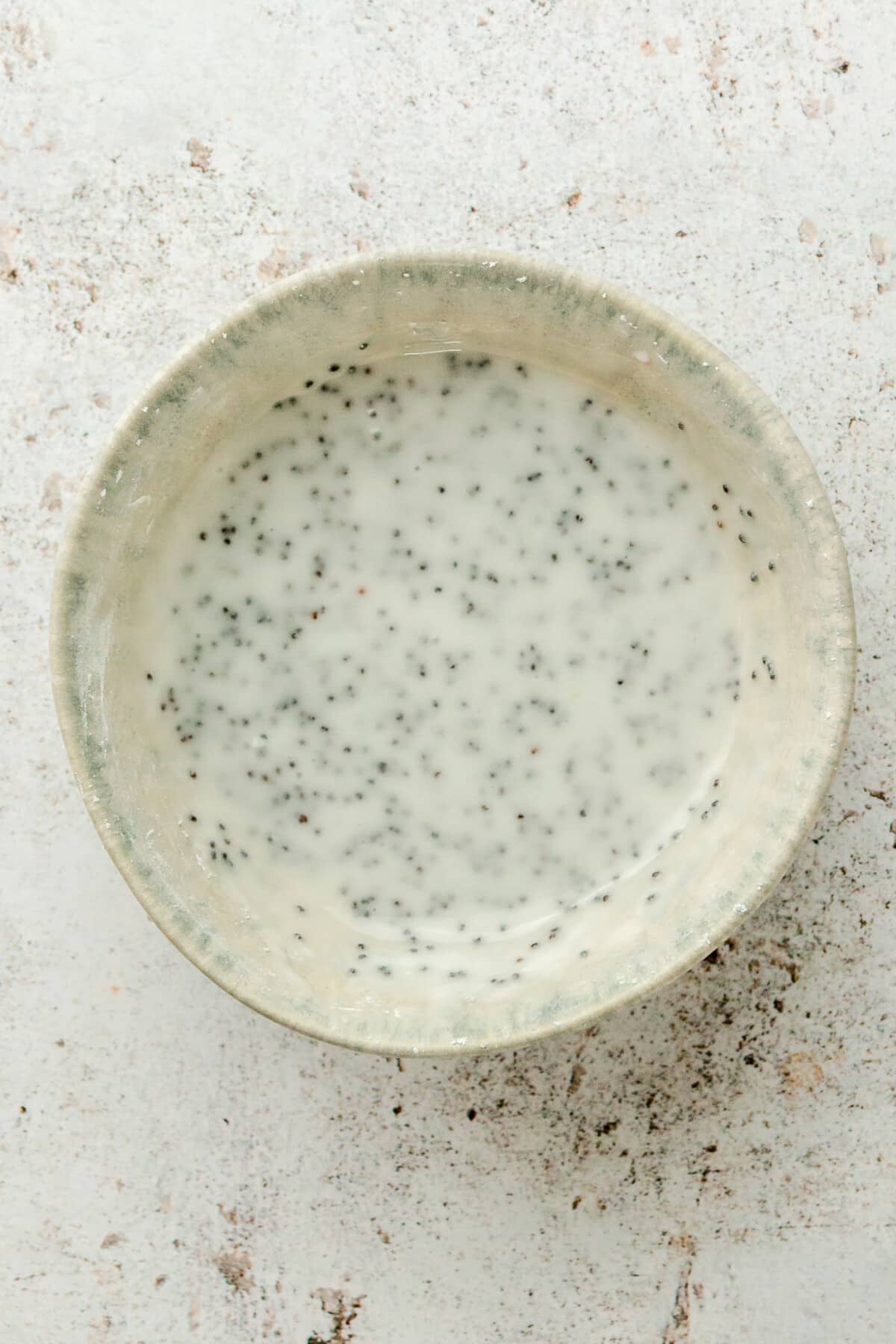 A lemon poppy seed glaze sits in a ceramic bowl on a light grey surface.