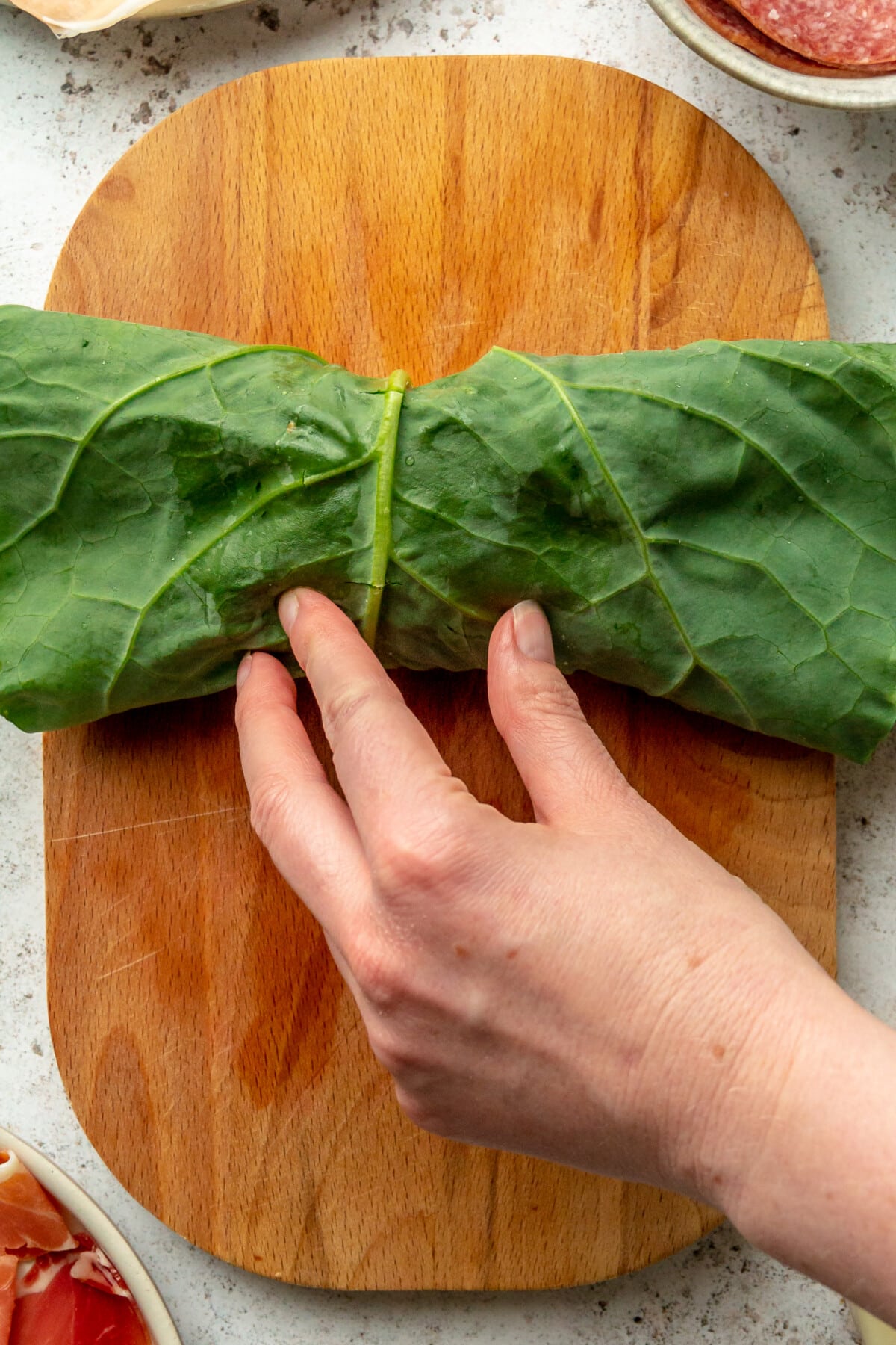 A collard green wrap is rolled on a small wooden board on a light grey surface.