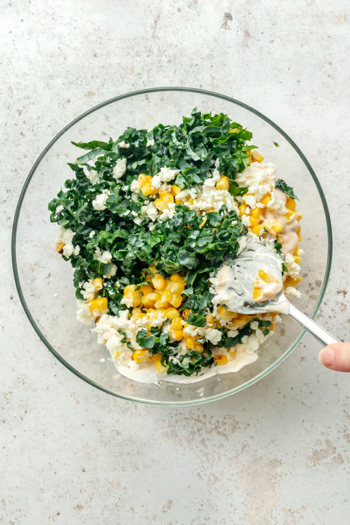 Mexican street corn and kale slaw is tossed with a mayo dressing in a bowl on a light grey surface.