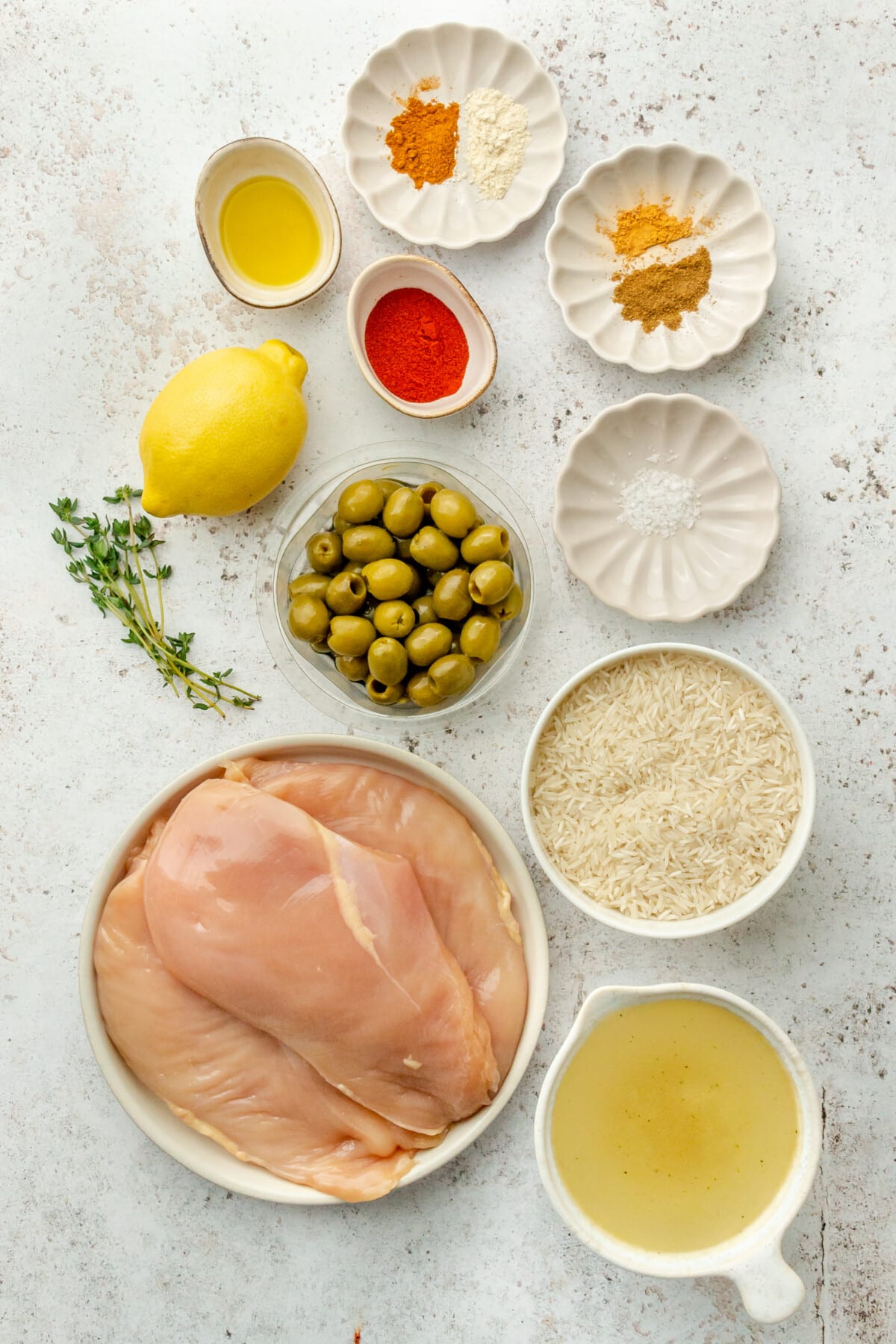 Ingredients for Moroccan inspired chicken with rice sit in a variety of plates and bowls on a light grey surface.