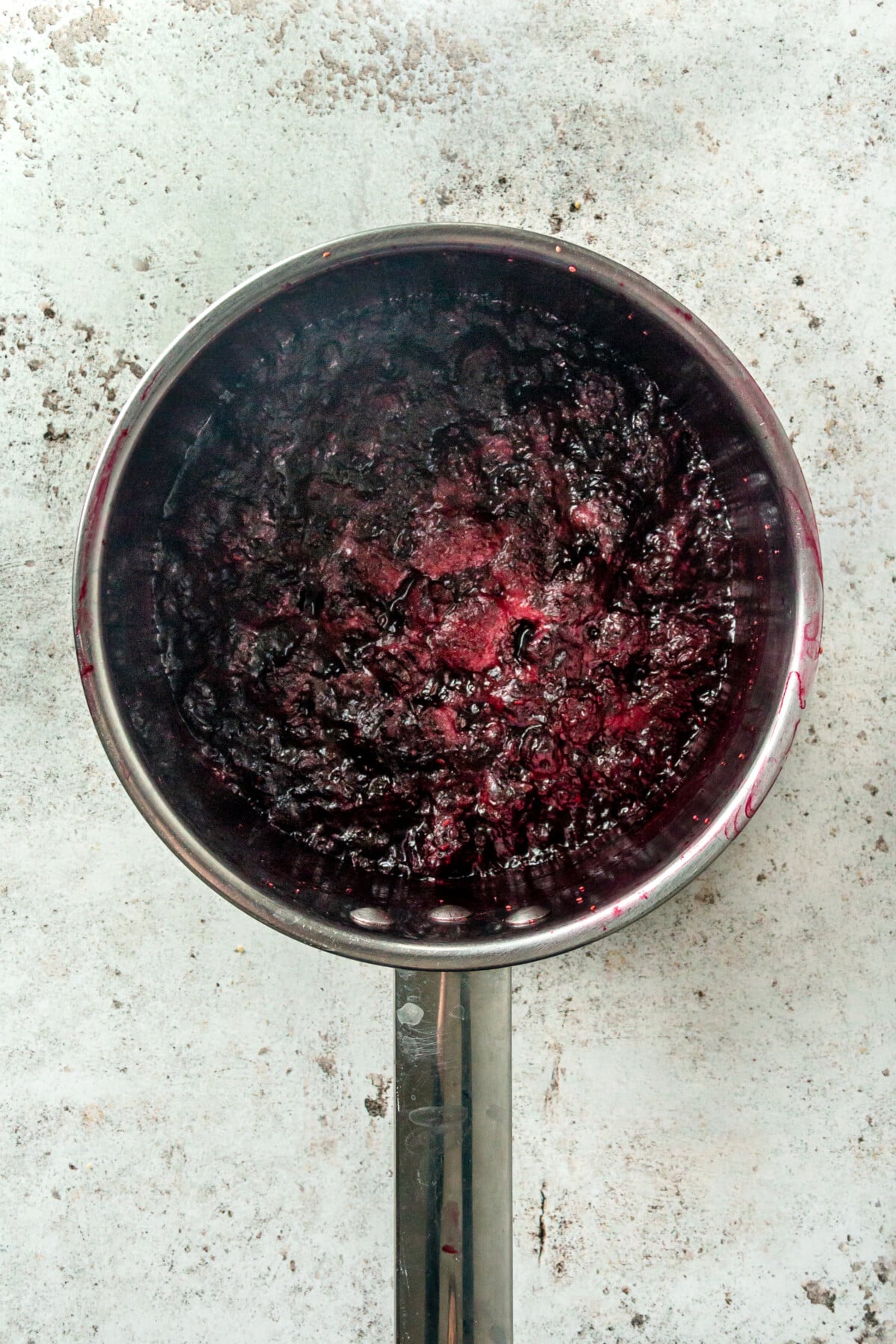 The berries are shown being cooked in the metal pot to create a dark purple mixture.