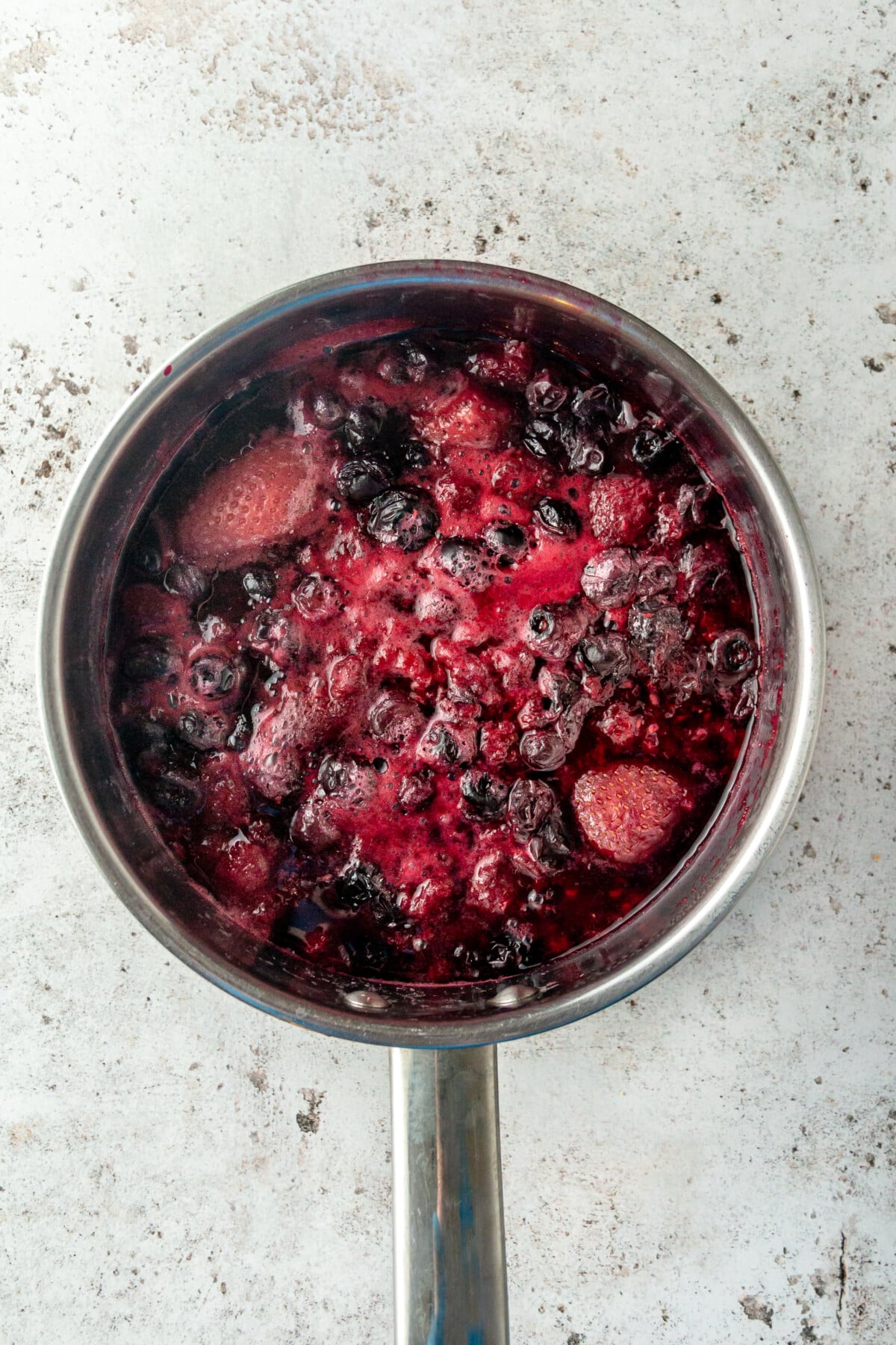A person using a masher to make homemade triple berry jam.