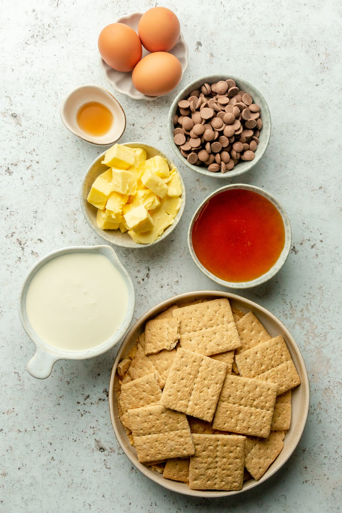Ingredients for old fashion chocolate mousse pie sit in a variety of bowls and plates on a light grey surface.