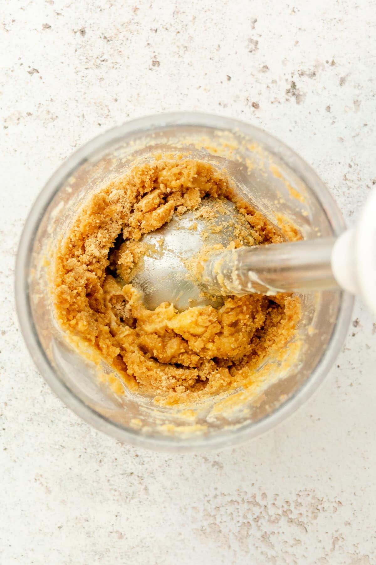 Crushed graham crackers are combined with softened butter in a blender beaker on a light gray surface.