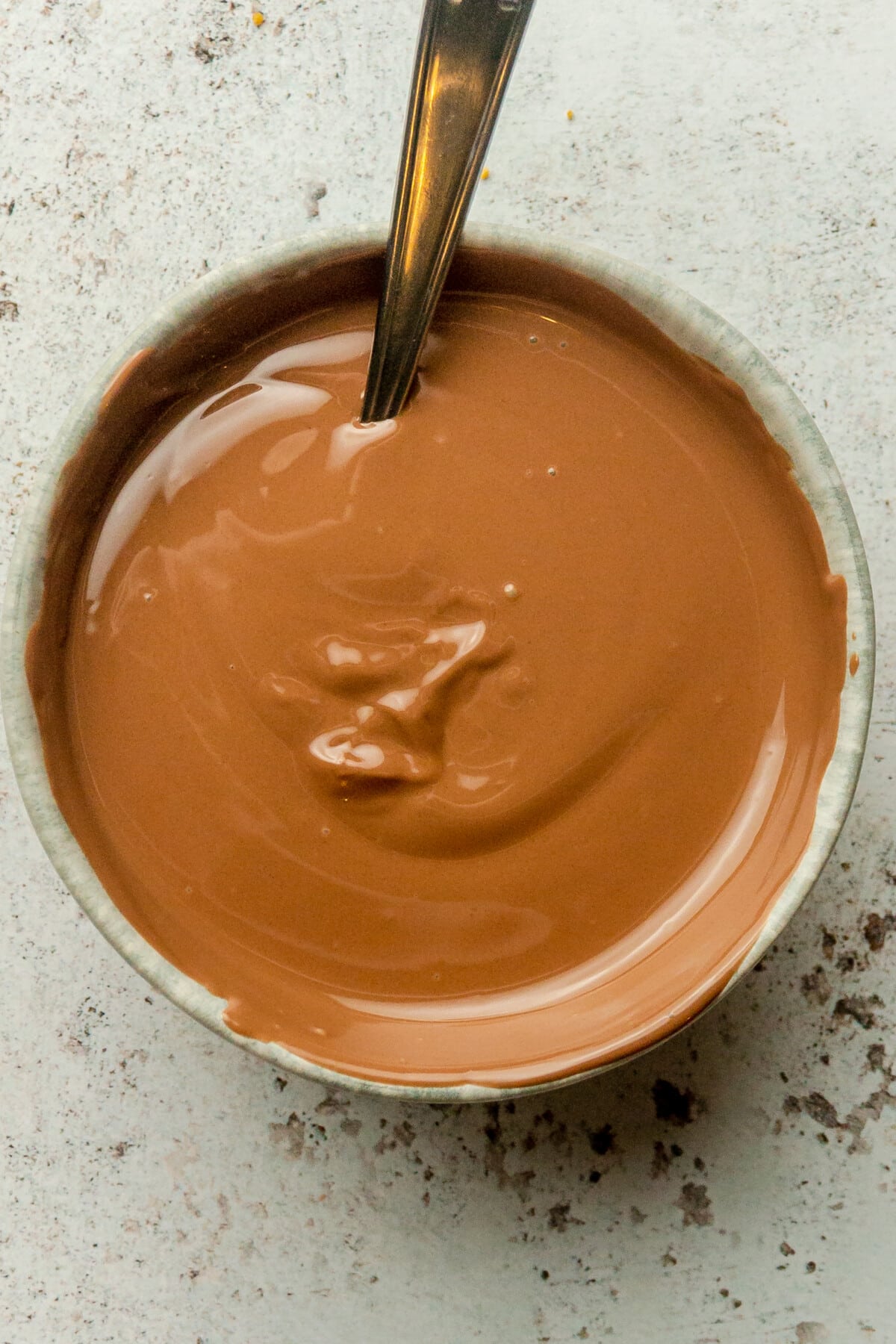 Melted chocolate sits in a blue ceramic bowl on a light gray surface.