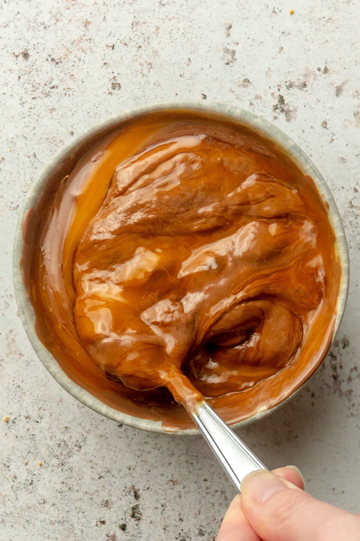 Melted chocoate and eggs are stirred in a blue ceramic bowl on a light gray surface.