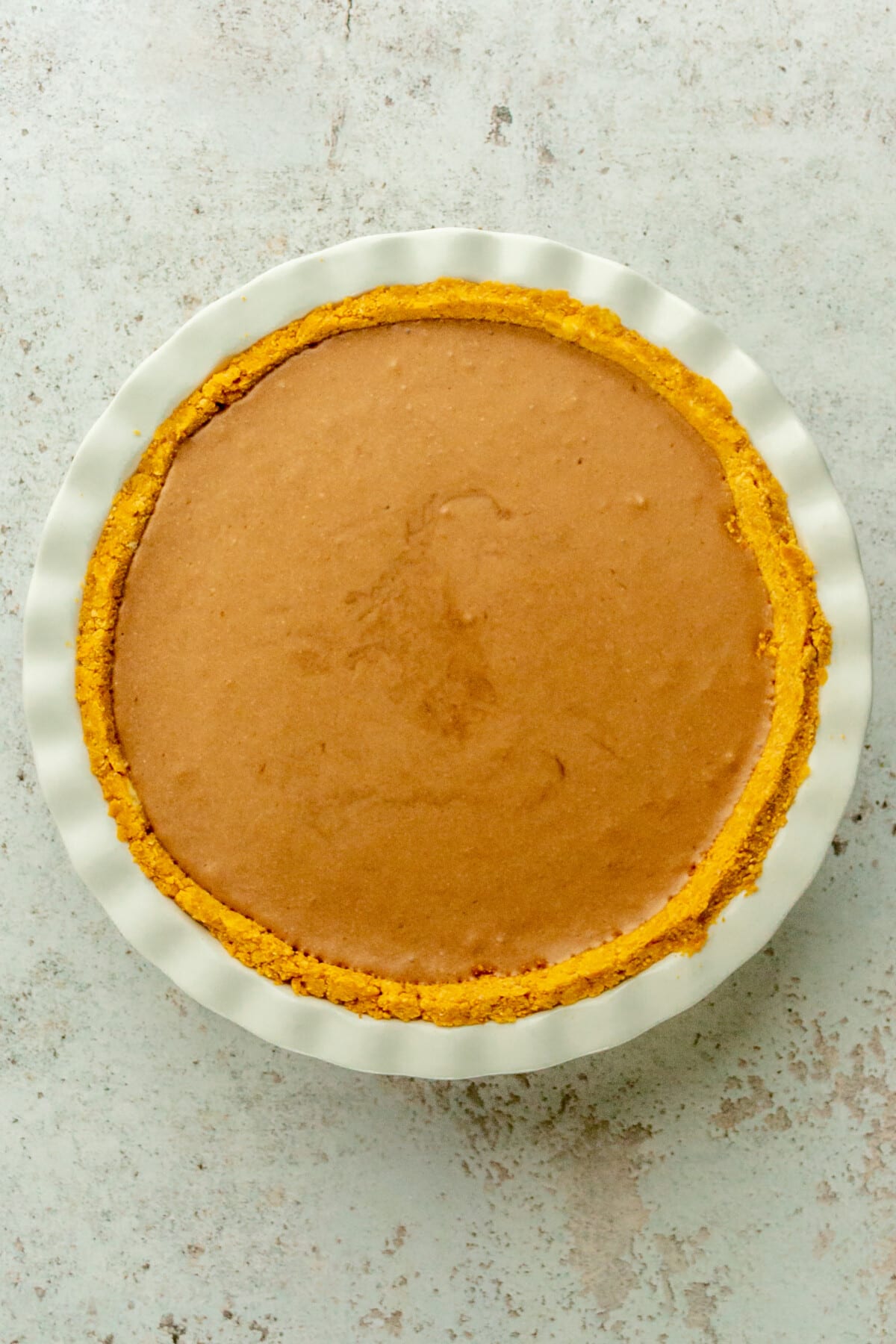 A no bake chocolate mousse pie sits in a white ceramic baking dish on a light gray surface.