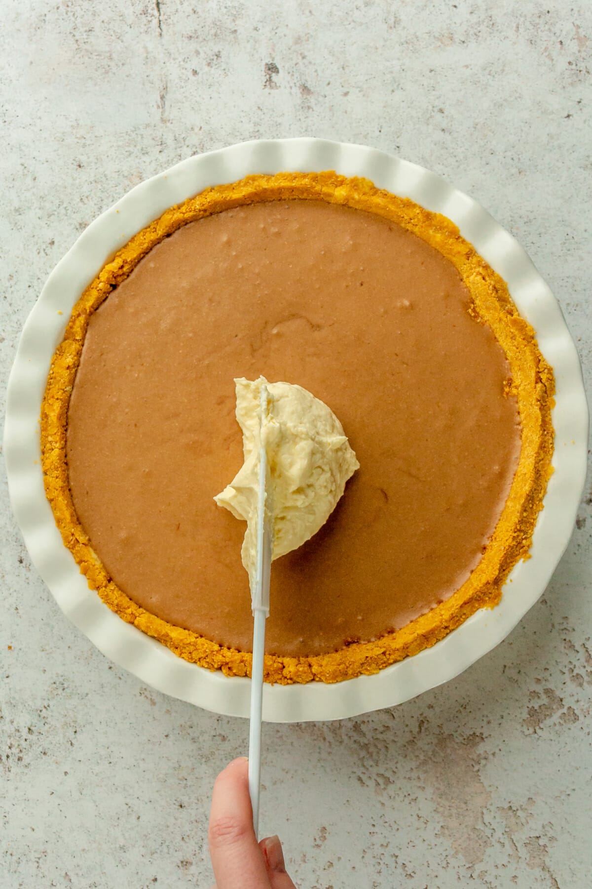 Whipped honey cream is placed on top of a chocolate mousse pie in a white ceramic pie dish on a light gray surface.