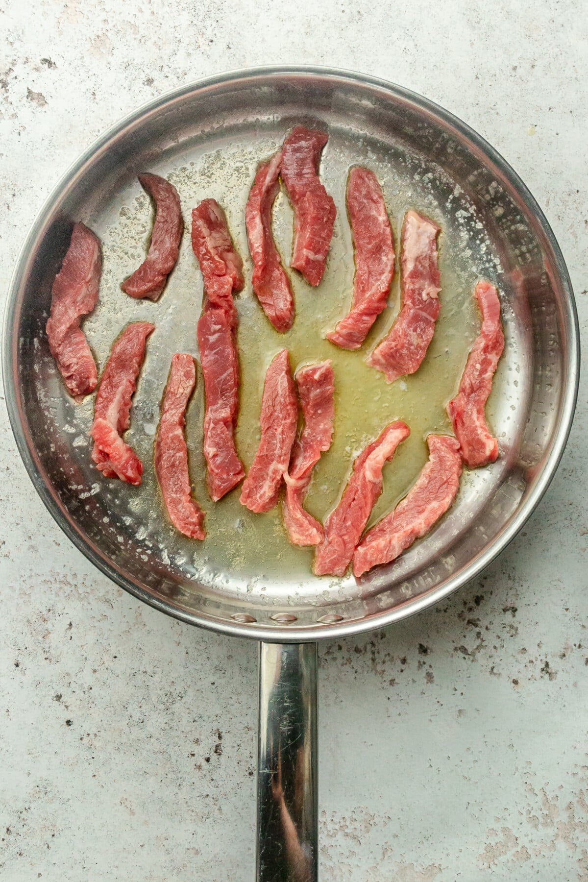 Pieces of beef sit in a stainless steel saucepan on a light gray surface.