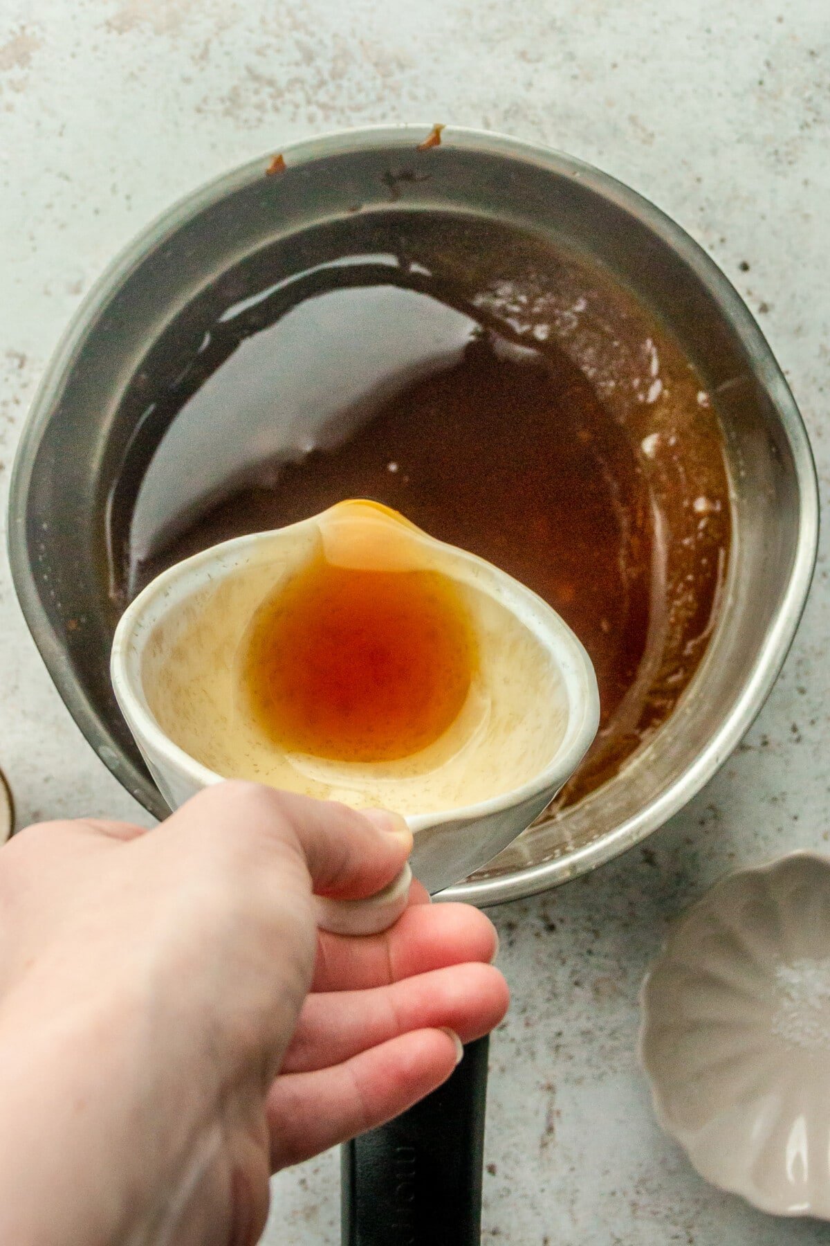 Maple syrup is poured over a melted butter and coconut sugar mixture on a light gray surface.